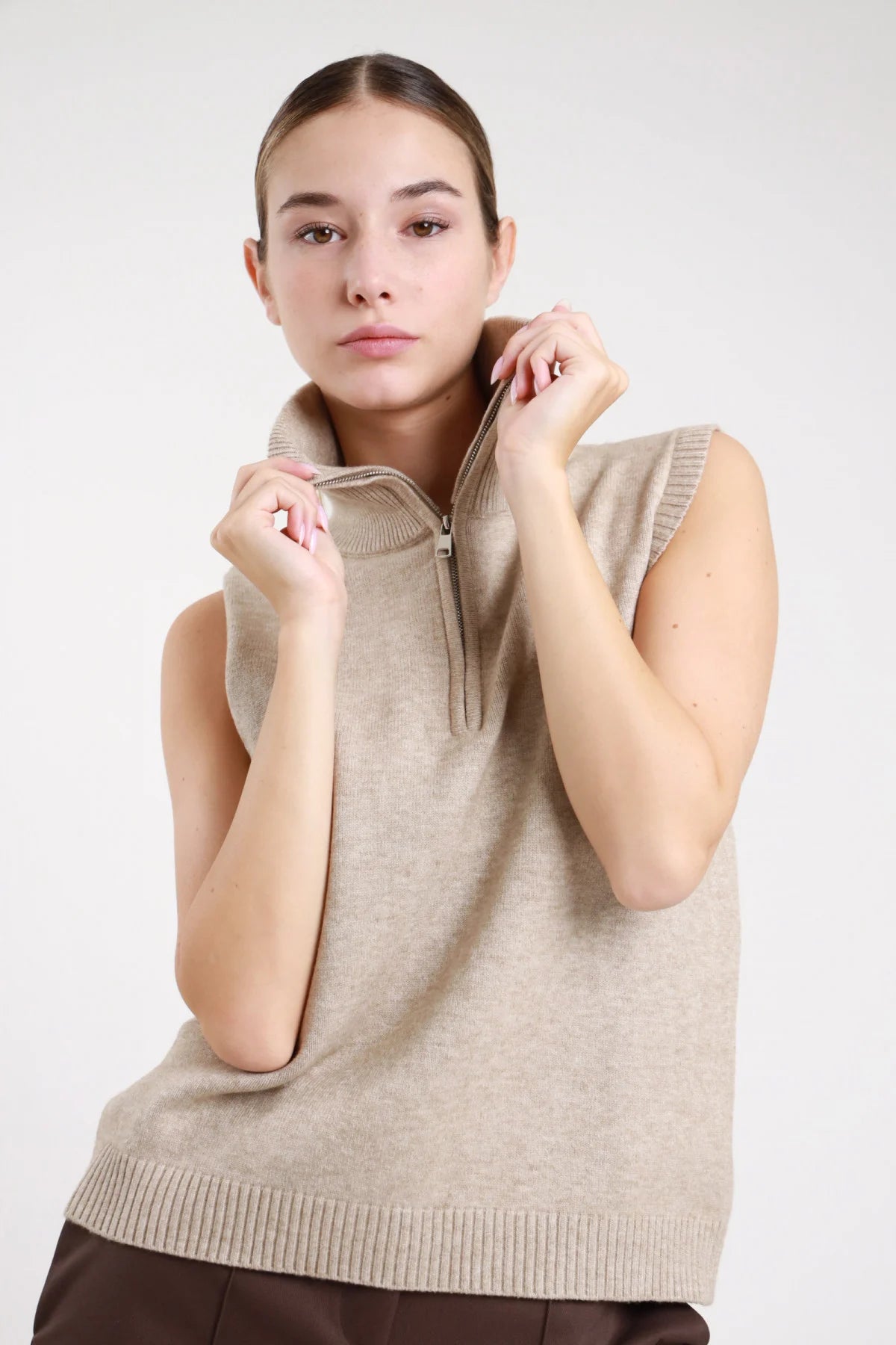 Gilet zip maglia sabbia cammello collo alto - modella busto frontale mani sul collo zip aperta sguardo frontale pantaloni marroni