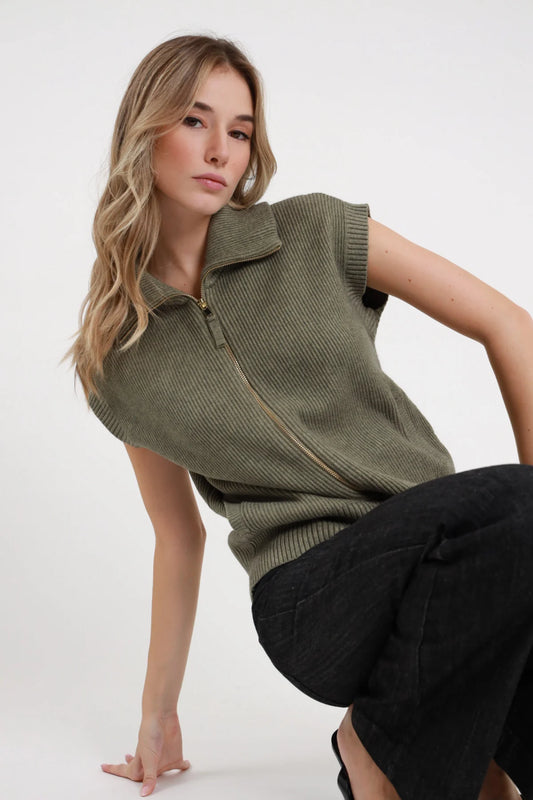 Gilet Costa Inglese Zip verde militare oliva 50% viscosa costa inglese zip dorata aperta V colletto polo cap sleeve dettaglio 3/4 laterale seduta posa dinamica - modella 3/4 laterale seduta posa dinamica sguardo 3/4 capelli biondi mossi sfondo bianco pantaloni cargo neri antracite abbinati
