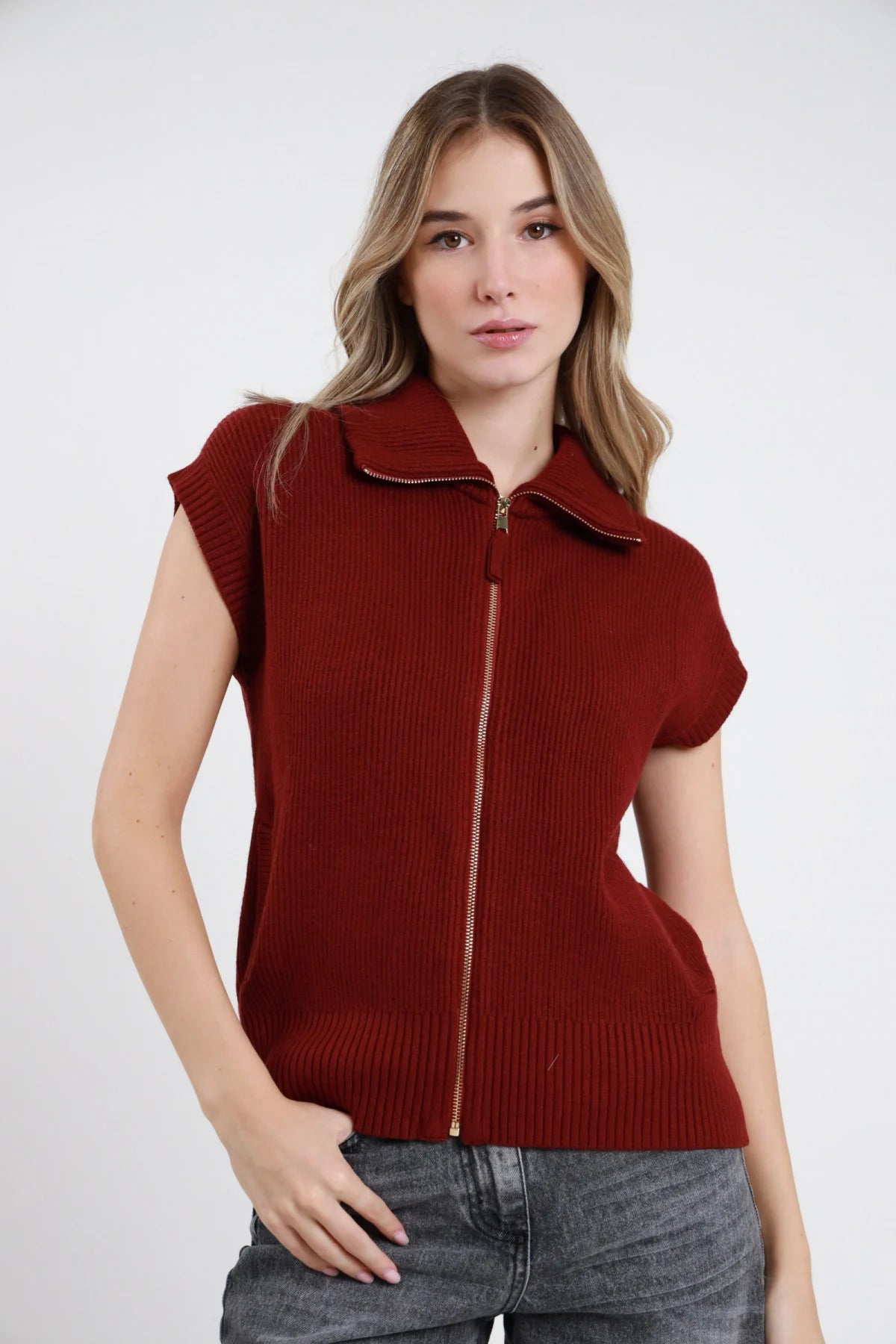 Gilet Costa Inglese Zip cioccolato marrone scuro 50% viscosa costa inglese colletto polo zip dorata cap sleeve boxy frontale busto mano orecchio - modella busto frontale mano orecchio sguardo laterale 3/4 capelli biondi mossi sfondo bianco pantaloni ecopelle nera abbinati