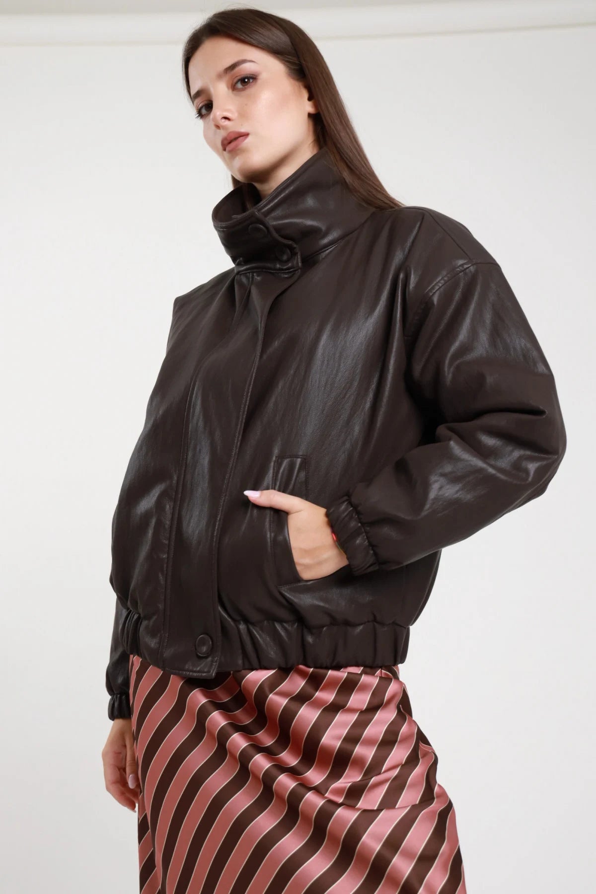 Bomber imbottito ecopelle marrone cioccolato donna oversize tasche laterali patta fondo elasticizzato - vista tre quarti laterale mano in tasca con gonna a righe rosa bordeaux