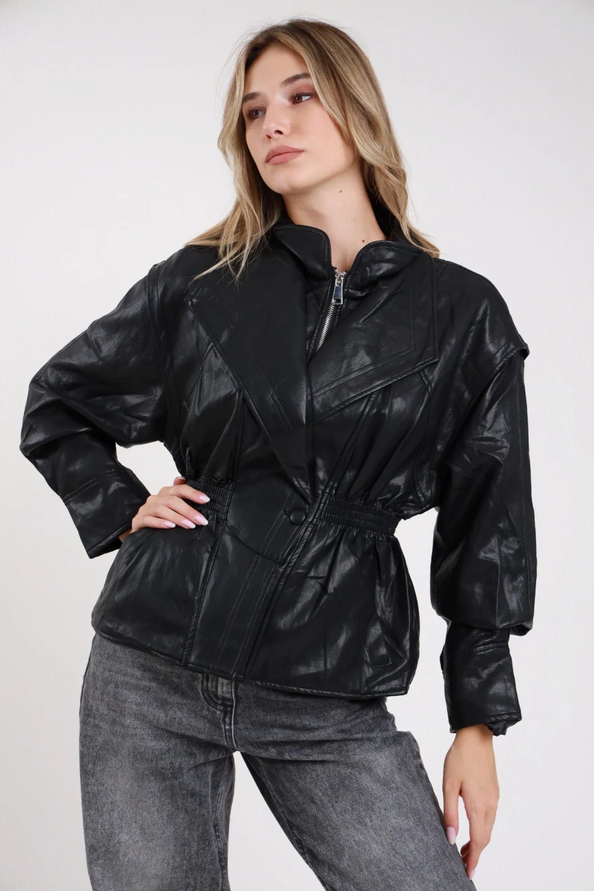Giacca ecopelle nera cuciture geometriche zip argentata vita smock - modella busto tre quarti mano sul fianco sguardo laterale jeans grigi capelli biondi mossi