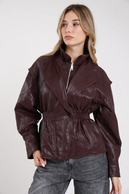 Giacca ecopelle bordeaux vino cuciture diagonali vita smock effetto peplum - modella frontale intera zip chiusa jeans grigi sguardo laterale capelli biondi mossi