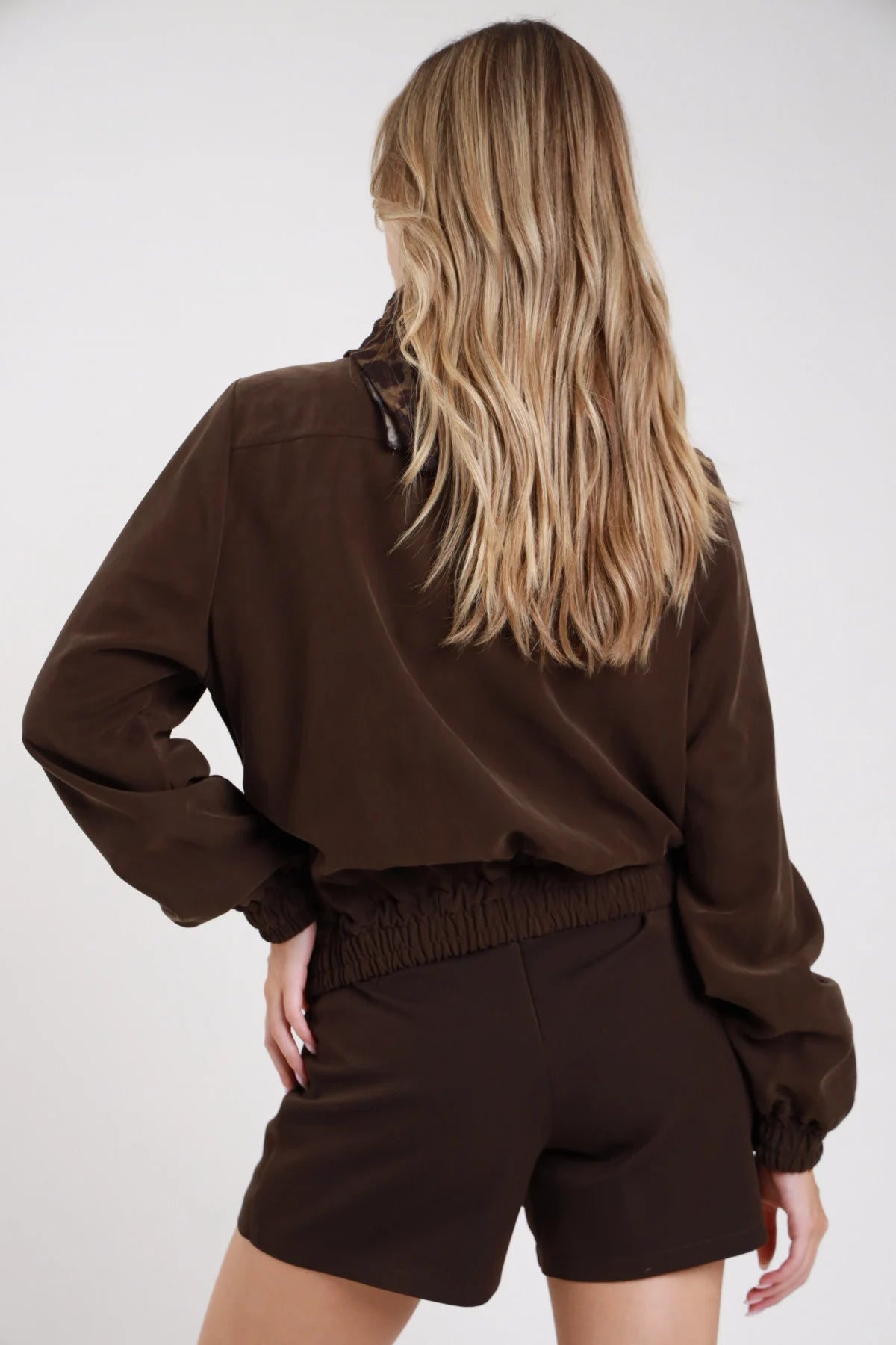 Giacca bomber viscosa suede melanzana prugna frontale mani fianchi foulard satin animalier annodato collo alto funnel neck snap abbottonatura - modella frontale mani fianchi foulard leopard annodato sguardo frontale pantaloni cioccolato capelli castani raccolti