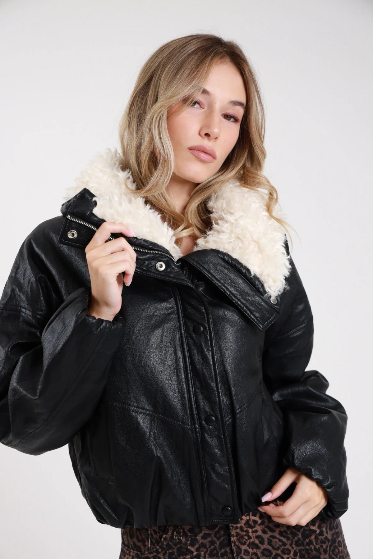 Giacca ecopelle nera collo revers maxi ecopelliccia boucle panna frontale busto tre quarti mani zip dettaglio zip frontale bottoni pressione argento manica batwing oversize - modella frontale busto tre quarti mani zip sguardo frontale pantaloni animalier leopard capelli biondi mossi