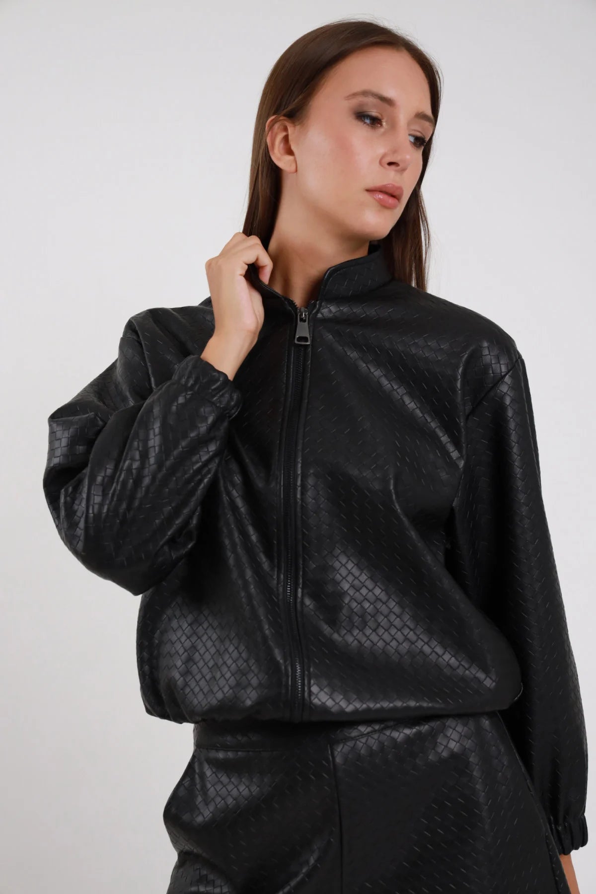 Bomber Ecopelle Intrecciato nero woven embossed romboidale oversize boxy crop zip chiusa tono su tono mano colletto manica balloon polsino arricciato busto frontale 3/4 - modella busto frontale 3/4 mano colletto sguardo abbasso capelli castani lisci sfondo bianco pantalone coordinato nero