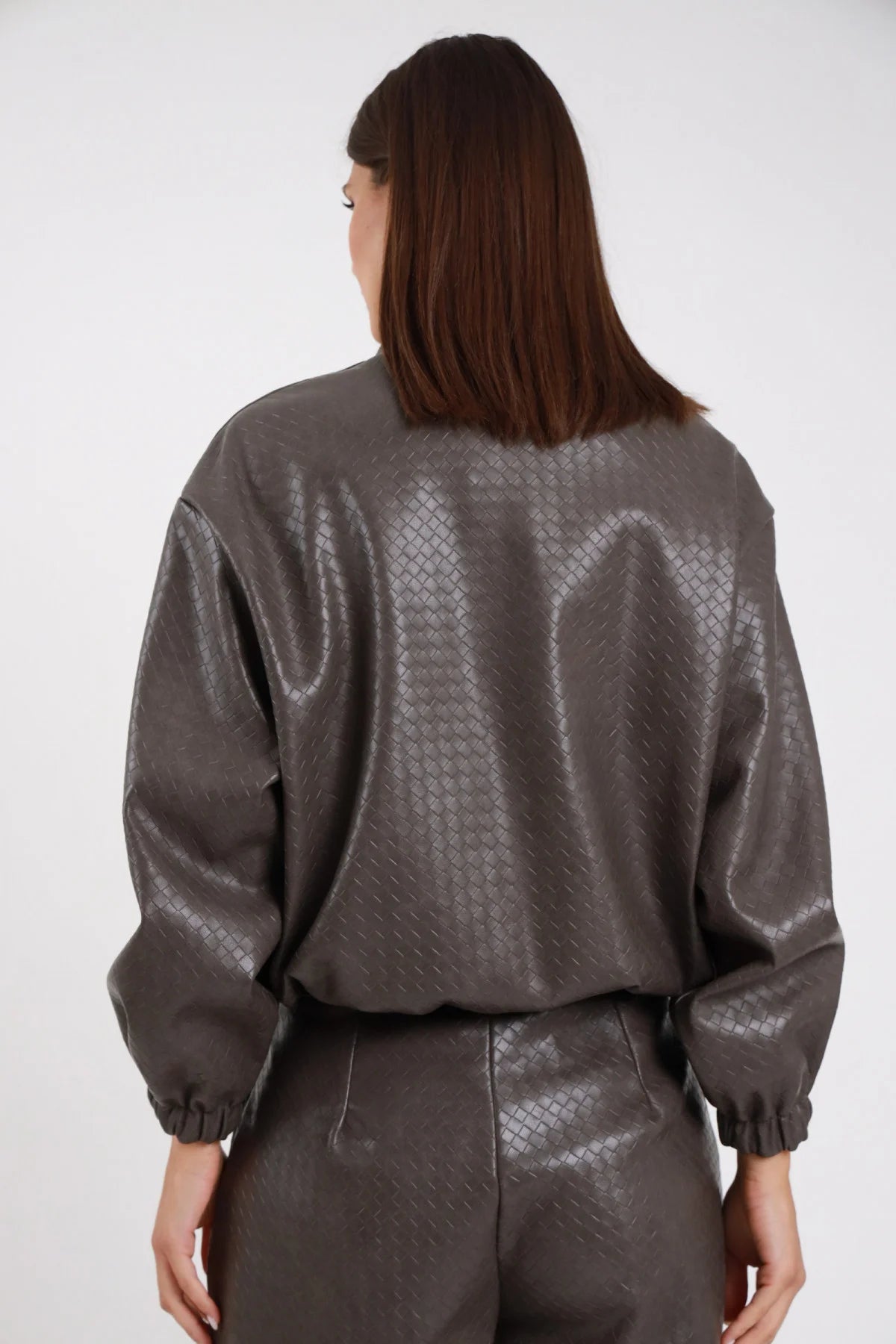 Bomber Ecopelle Intrecciato grigio talpa taupe woven embossed romboidale oversize boxy crop texture intrecciata schiena manica balloon polsino elastico retro intera - modella retro intera braccia lungo corpo sguardo laterale capelli castani lisci sfondo bianco pantalone coordinato grigio