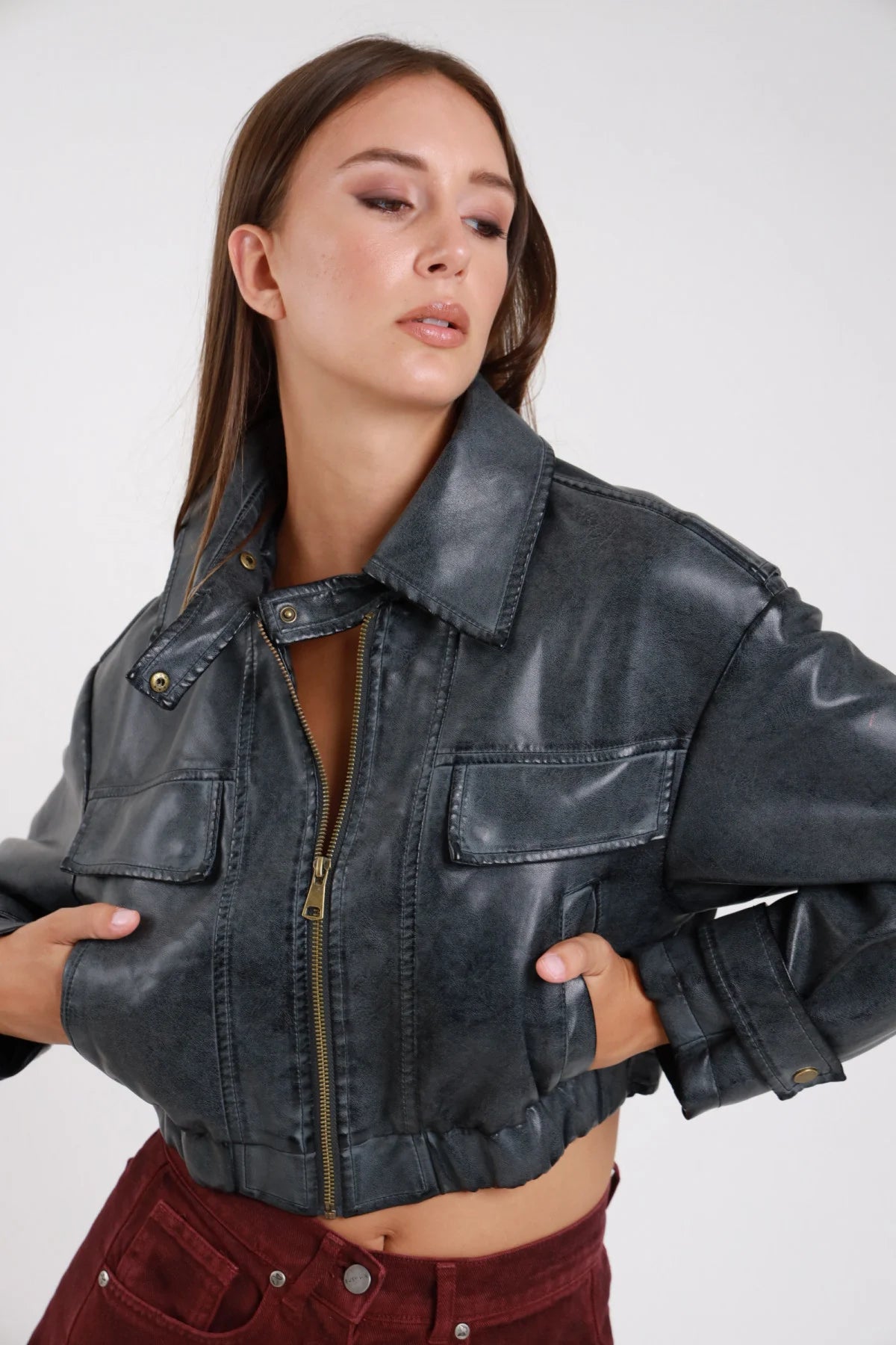 Bomber crop ecopelle washed ardesia busto tre quarti zip aperta cursore dorato bronzo colletto strutturato tasche toppa petto - modella busto tre quarti mani vita zip aperta sguardo basso laterale pantaloni borgogna capelli castani lisci