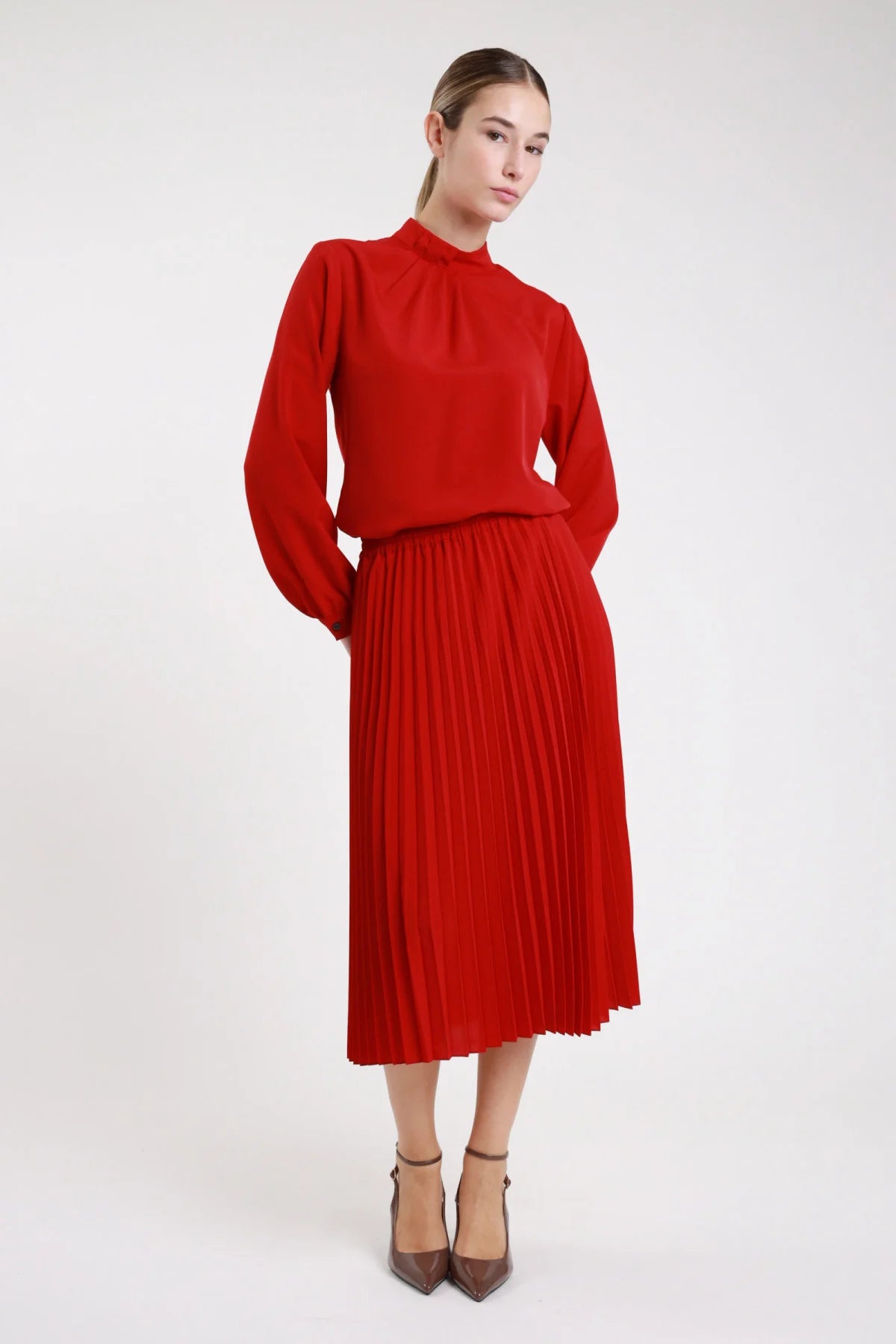 Gonna plissettata midi rosso vita elastica plissé fitto - modella frontale intera con blusa abbinata colletto alto e décolleté grigi capelli castani lisci sguardo frontale