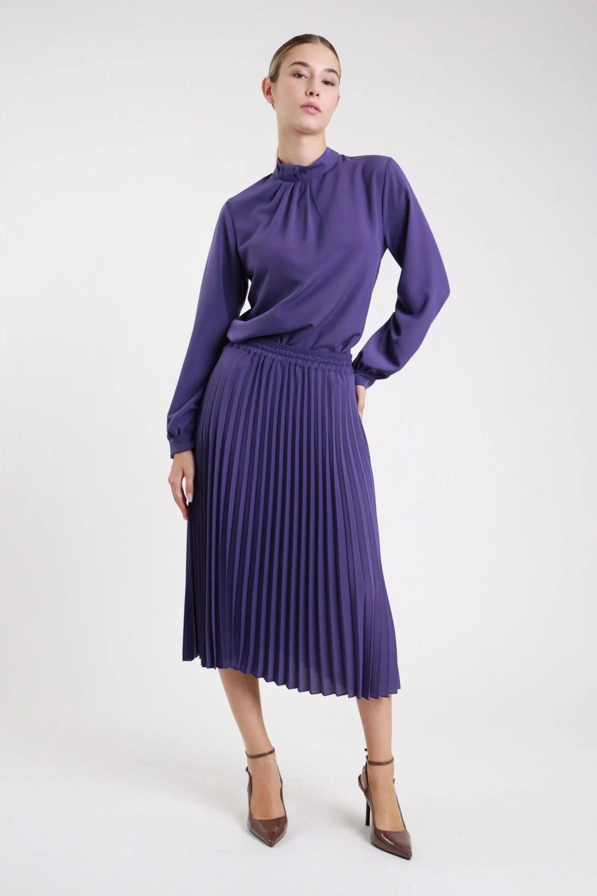 Gonna plissettata midi viola indaco fluida svasata - modella frontale intera con blusa abbinata colletto alto e décolleté grigi capelli castani lisci sguardo frontale
