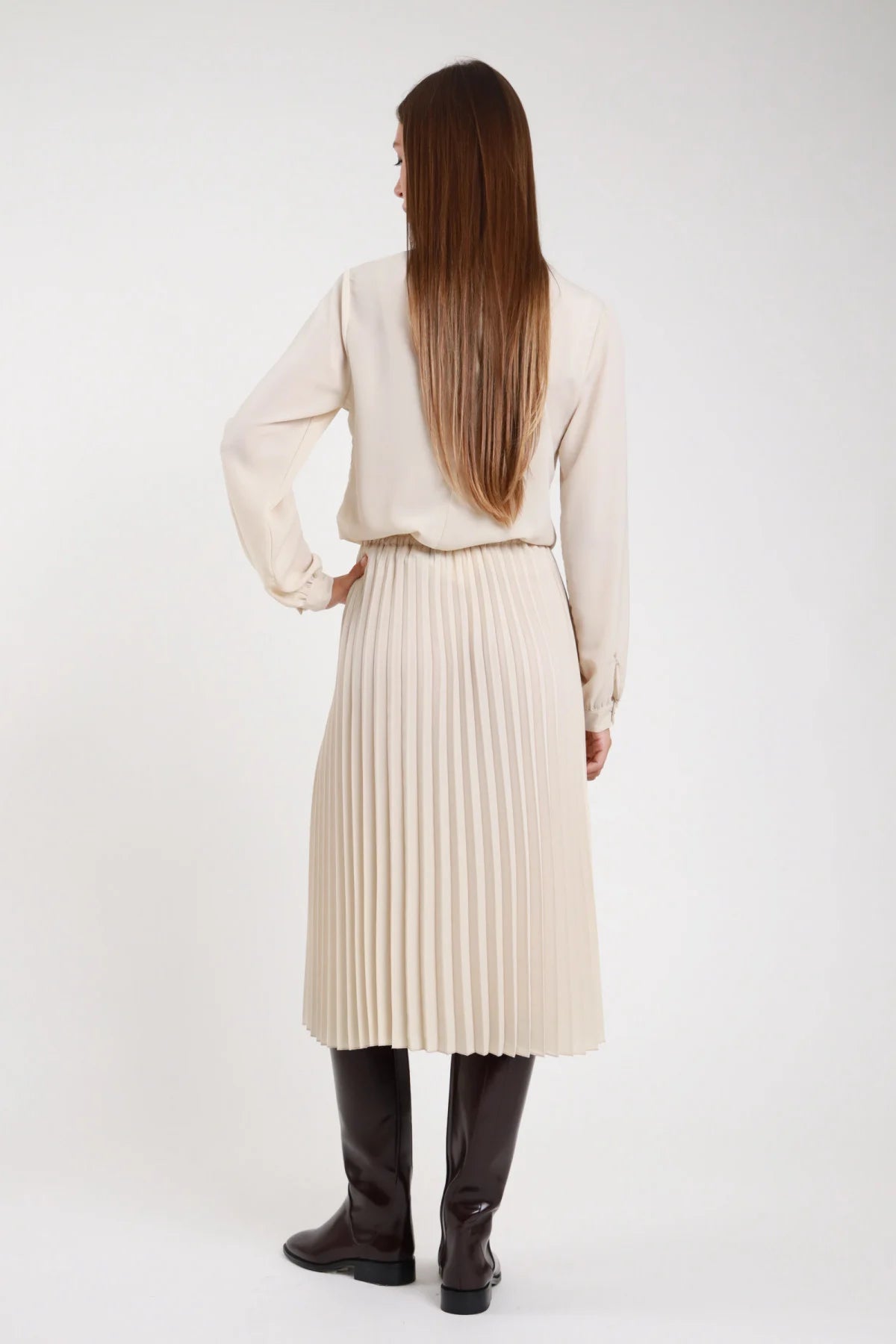 Gonna plissettata panna ecrù plissé regolare vita elastica retro - modella retro intera capelli lunghi lisci castani con stivali neri alti mano sul fianco