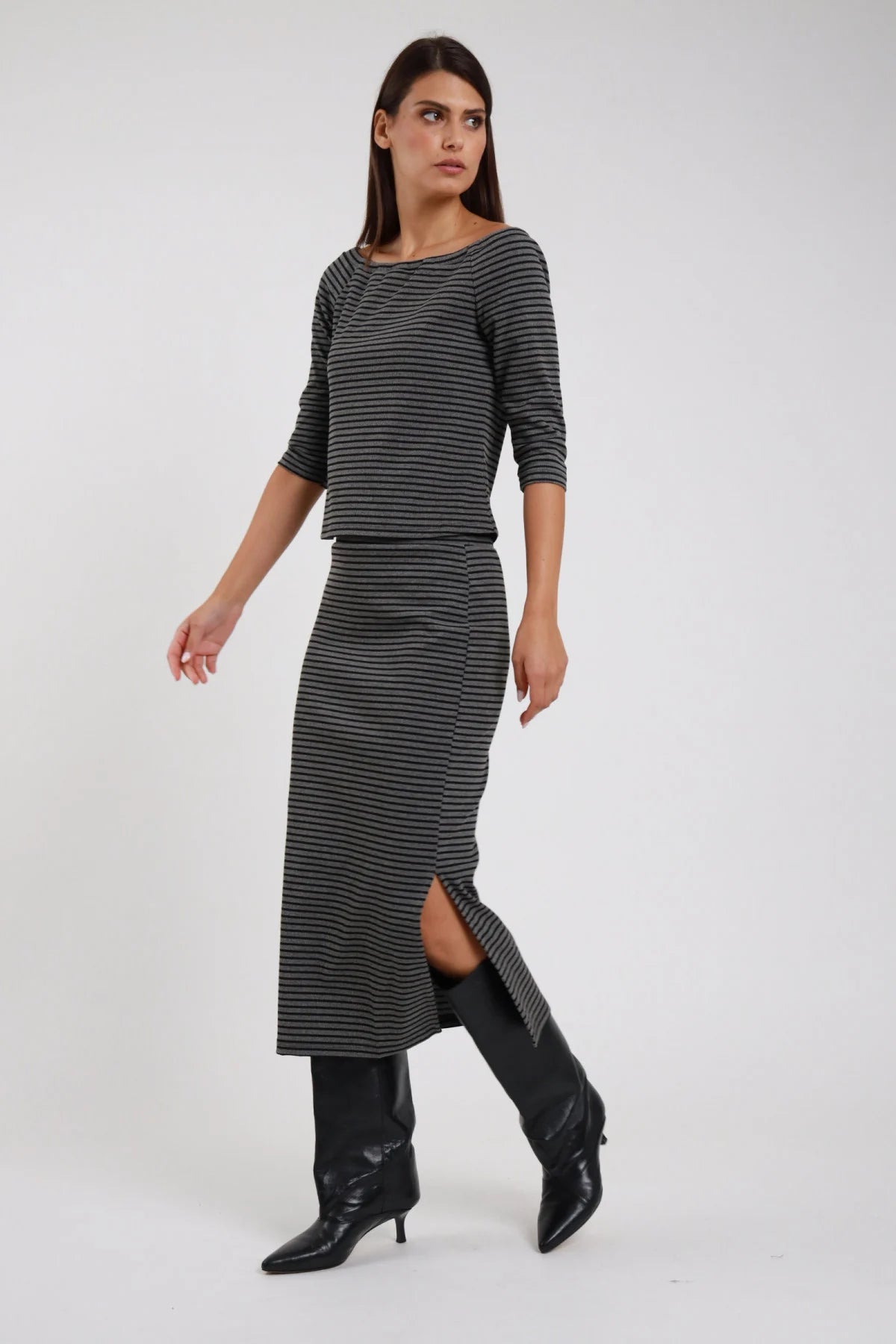 Gonna Midi Longuette Righe grigio antracite nero lurex 48% cotone elastico vita silhouette semi-aderente spacco laterale - modella intera laterale posa dinamica gamba avanzata sguardo laterale capelli castani lisci sfondo bianco top righe grigio coordinato stivali neri ginocchio tacco