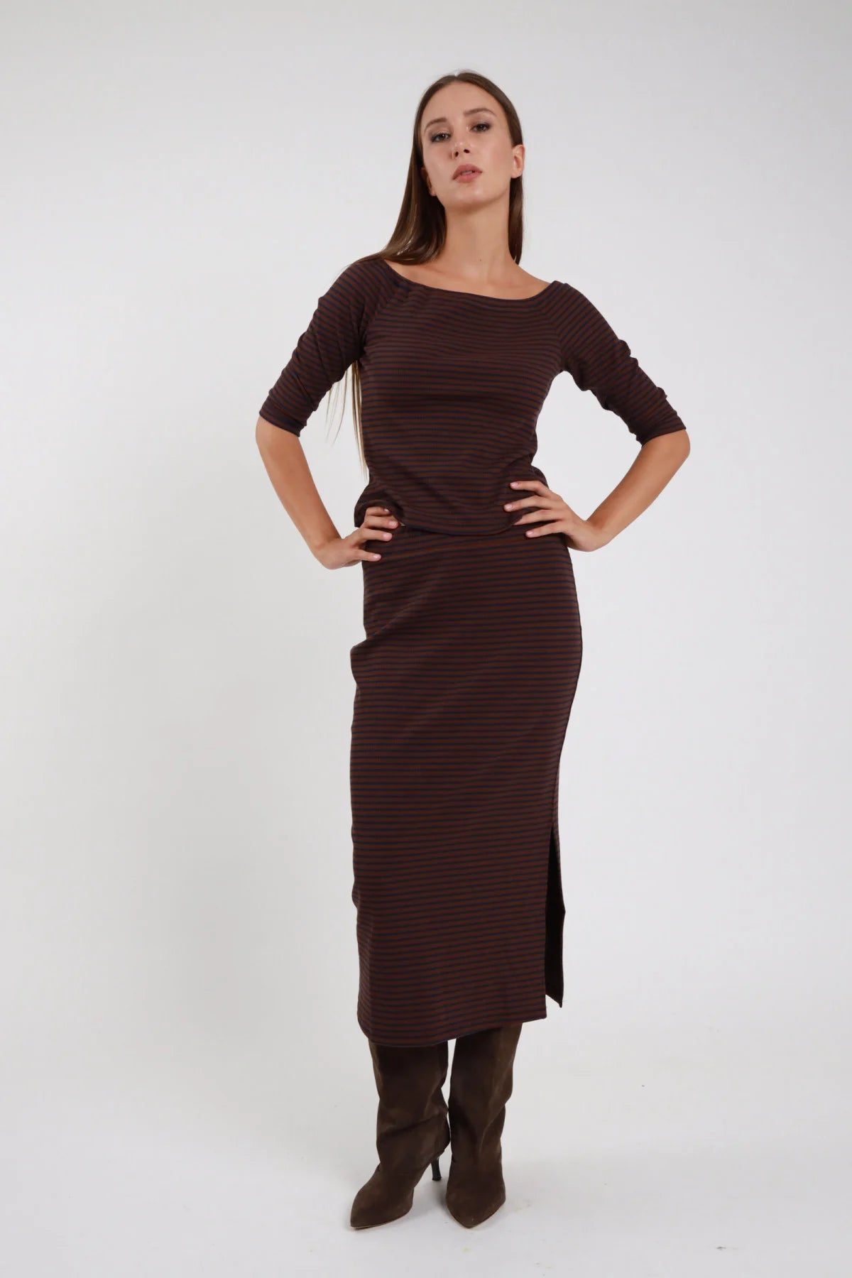Gonna Midi Longuette marrone cioccolato tinta unita 48% cotone elastico vita silhouette semi-aderente spacco laterale frontale - modella intera frontale posa statica mani fianchi sguardo frontale capelli castani lisci sfondo bianco top marrone coordinato stivali marrone