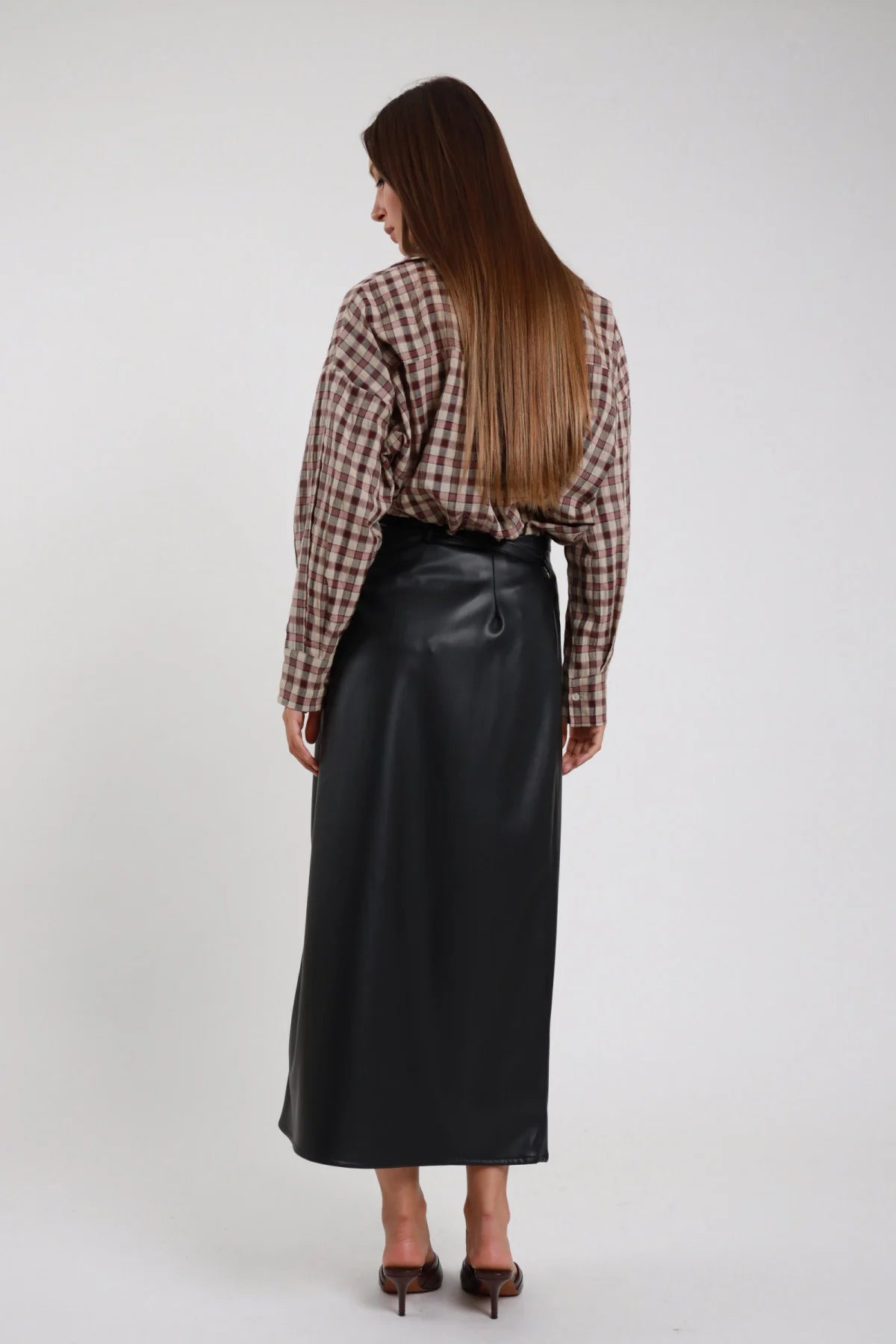 Gonna Ecopelle nero maxi dritta vita alta spacco frontale silhouette midi-lunga retro intera schiena - modella retro intera sguardo laterale capelli castani lisci sfondo bianco camicia check beige marrone oversize décolleté marroni tacco kitten