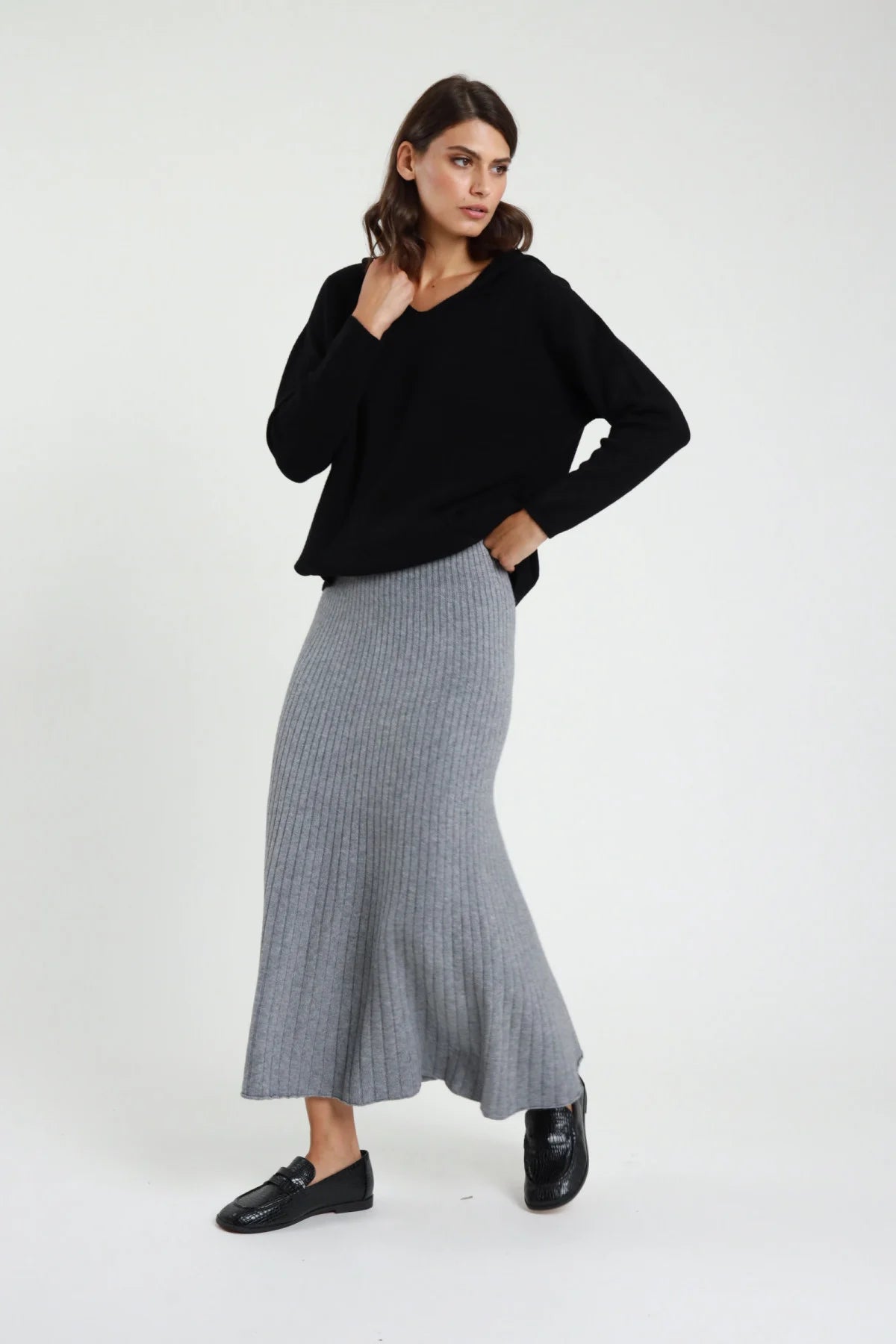 Gonna in Maglia coste ribbed grigio melange vita alta silhouette sirena mermaid midi-maxi orlo svasato frontale intera posa laterale - modella frontale intera posa laterale mano colletto sguardo laterale capelli castani sfondo bianco maglione nero scollo V loafer neri vernice