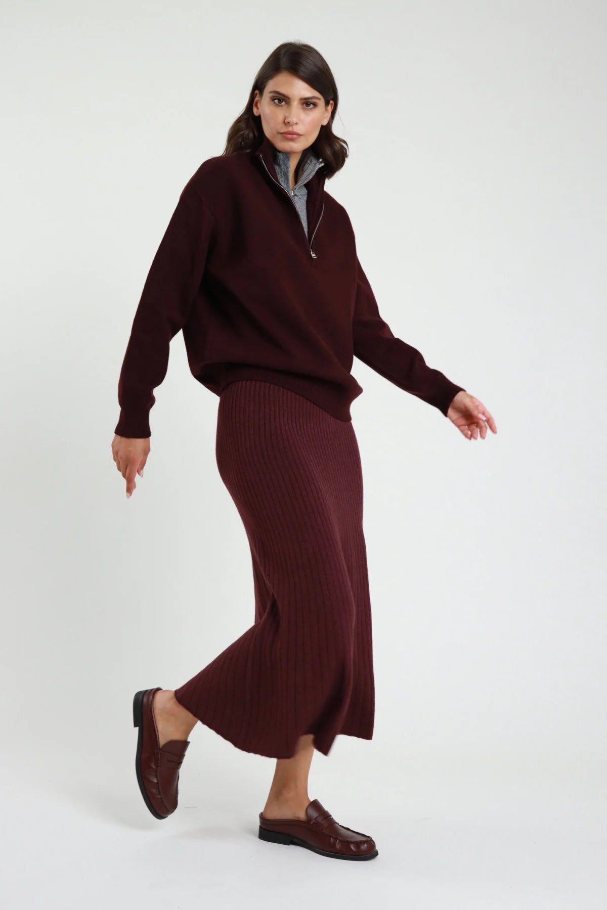 Gonna in Maglia coste ribbed bordeaux vinaccia vita alta silhouette sirena mermaid midi-maxi orlo svasato frontale intera posa dinamica - modella frontale intera posa dinamica sguardo laterale capelli castani sfondo bianco maglione bordeaux half-zip loafer bordeaux