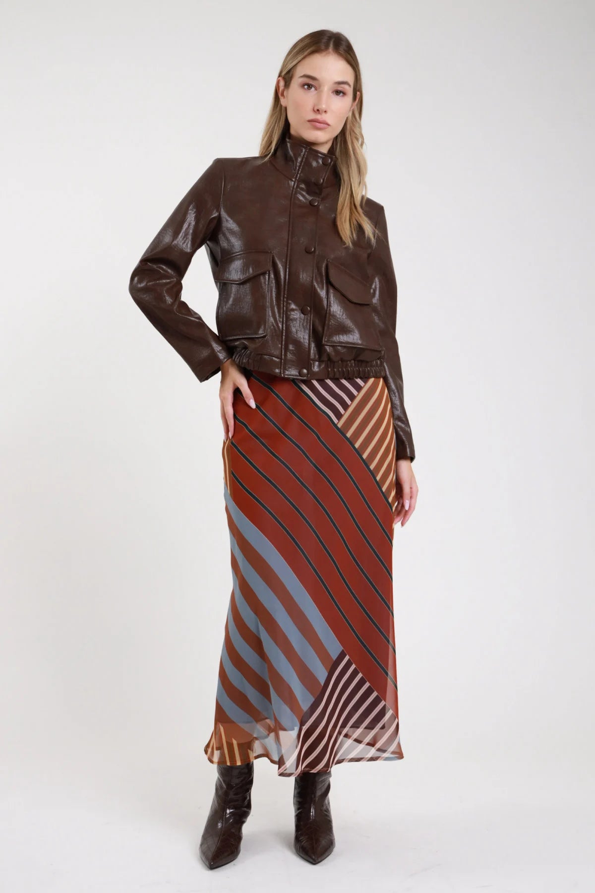 Gonna fantasia righe anni 70 terracotta azzurro tre quarti dinamica giacca pelle marrone - modella tre quarti passo dinamico sguardo frontale stivali croco tacco capelli biondi