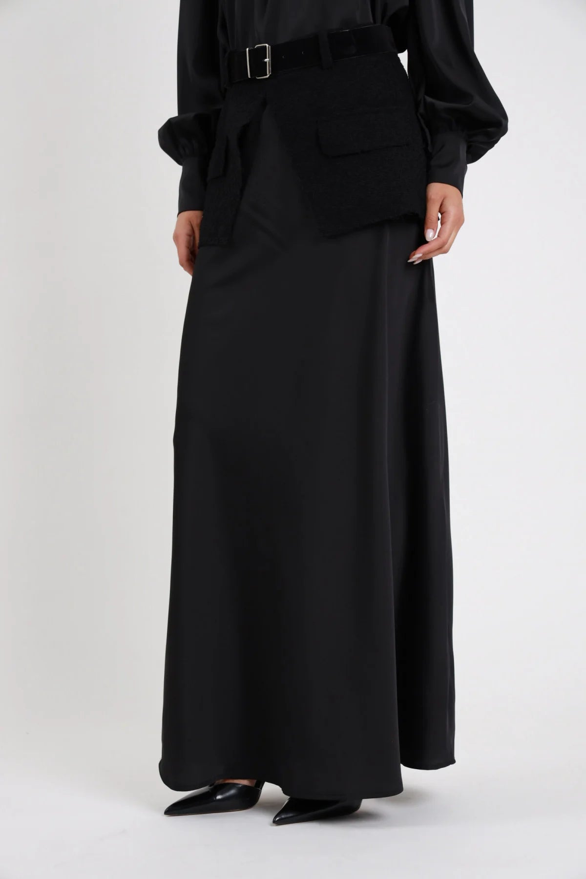 Gonna Lunga Cintura nera 100% poliestere satin lucido vita alta fascia maglia costina larga cintura pelle suede fibbia argento squadrata silhouette svasata flared maxi floor length dettaglio vita gamba frontale - modella vita gamba frontale mani laterali sfondo bianco camicia fiocco retro nera coordinata décolleté neri punta