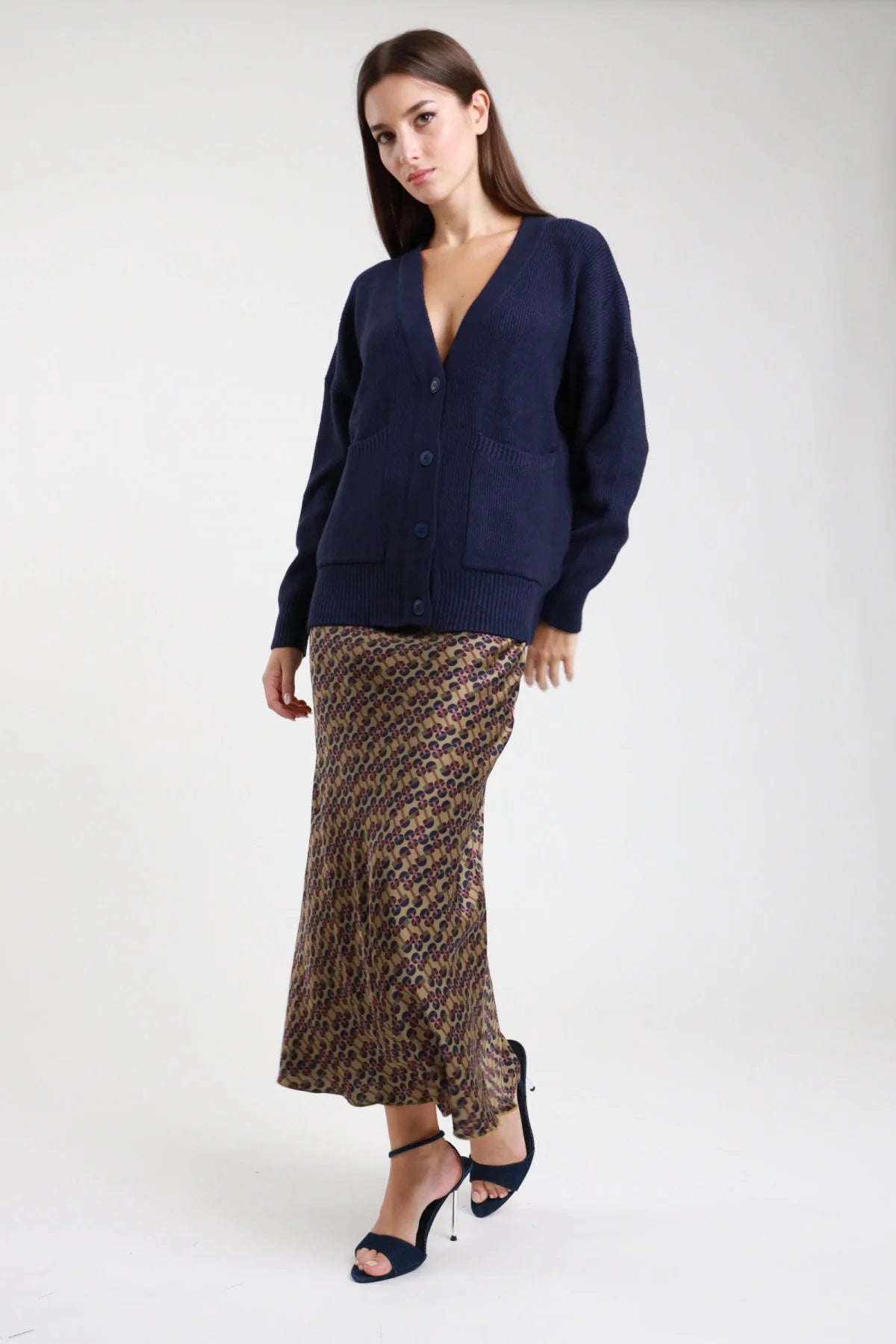 Gonna lunga fantasia geometrica retro anni 70 cachi marrone viola donna viscosa satinata vita alta elastico smock taglio tromba mermaid - vista frontale intera mano in tasca con cardigan navy e sandali tacco neri