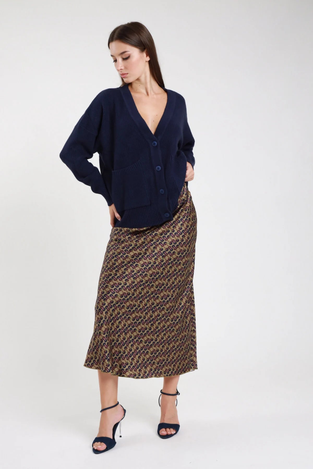 Gonna lunga fantasia geometrica retro cachi marrone viola donna viscosa satinata vita alta bias cut svasato fondo ondulato - vista frontale intera mani sui fianchi con cardigan navy e sandali tacco neri