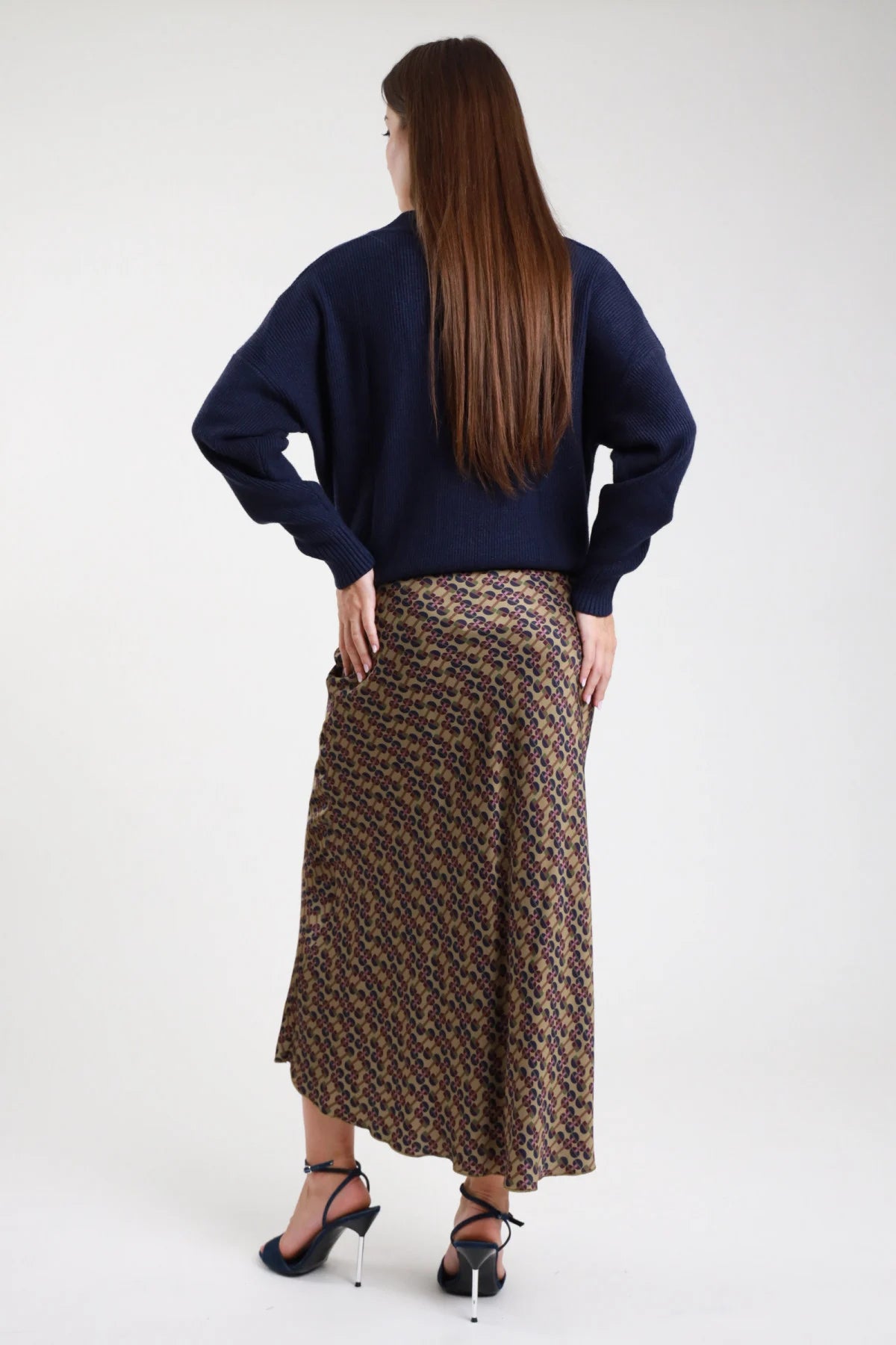 Gonna lunga fantasia geometrica retro anni 70 cachi marrone viola donna viscosa satinata taglio mermaid fondo ondulato fluido - vista posteriore intera mani sui fianchi con cardigan navy e sandali tacco neri