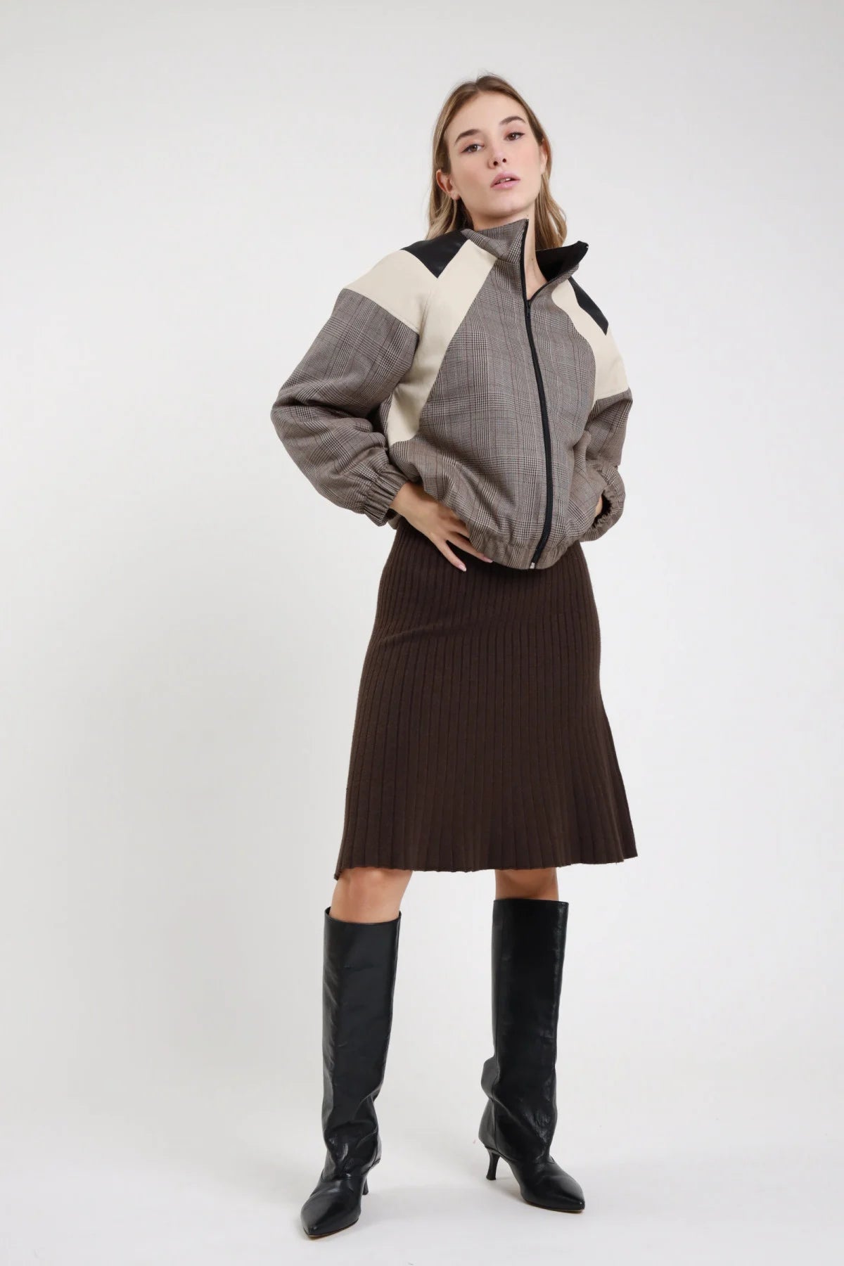 Gonna Midi Coste Plissé marrone cioccolato 52% viscosa coste verticali plissé fitte elastico vita invisibile silhouette A-line svasata lunghezza midi ginocchio - modella intera 3/4 frontale posa mano fianco sguardo 3/4 soft capelli biondi mossi sfondo bianco bomber prince of wales grigio panna nero stivali neri tacco