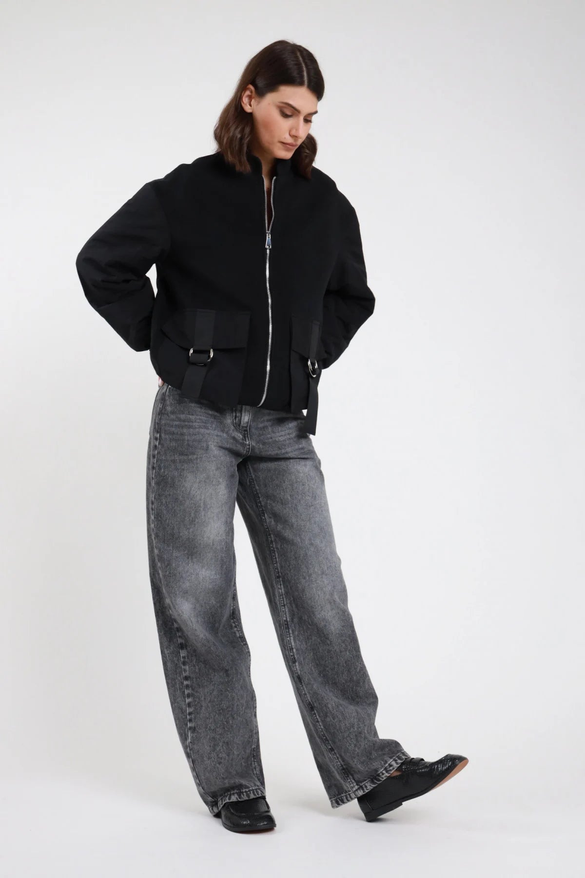 Jeans Mire straight leg wide leg grigio antracite stonewashed vita alta 5 tasche gamba larga maxi orlo grezzo frontale intera posa mossa sguardo basso - modella frontale intera posa mossa sguardo basso capelli castani scuri sfondo bianco bomber nero zip argento loafer neri