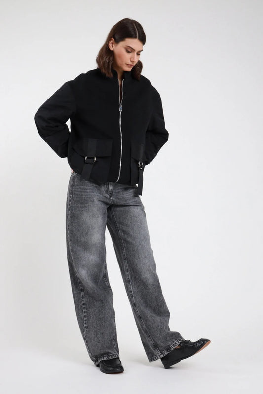 Jeans Mire straight leg wide leg grigio antracite stonewashed vita alta 5 tasche gamba larga maxi orlo grezzo frontale intera posa mossa sguardo basso - modella frontale intera posa mossa sguardo basso capelli castani scuri sfondo bianco bomber nero zip argento loafer neri