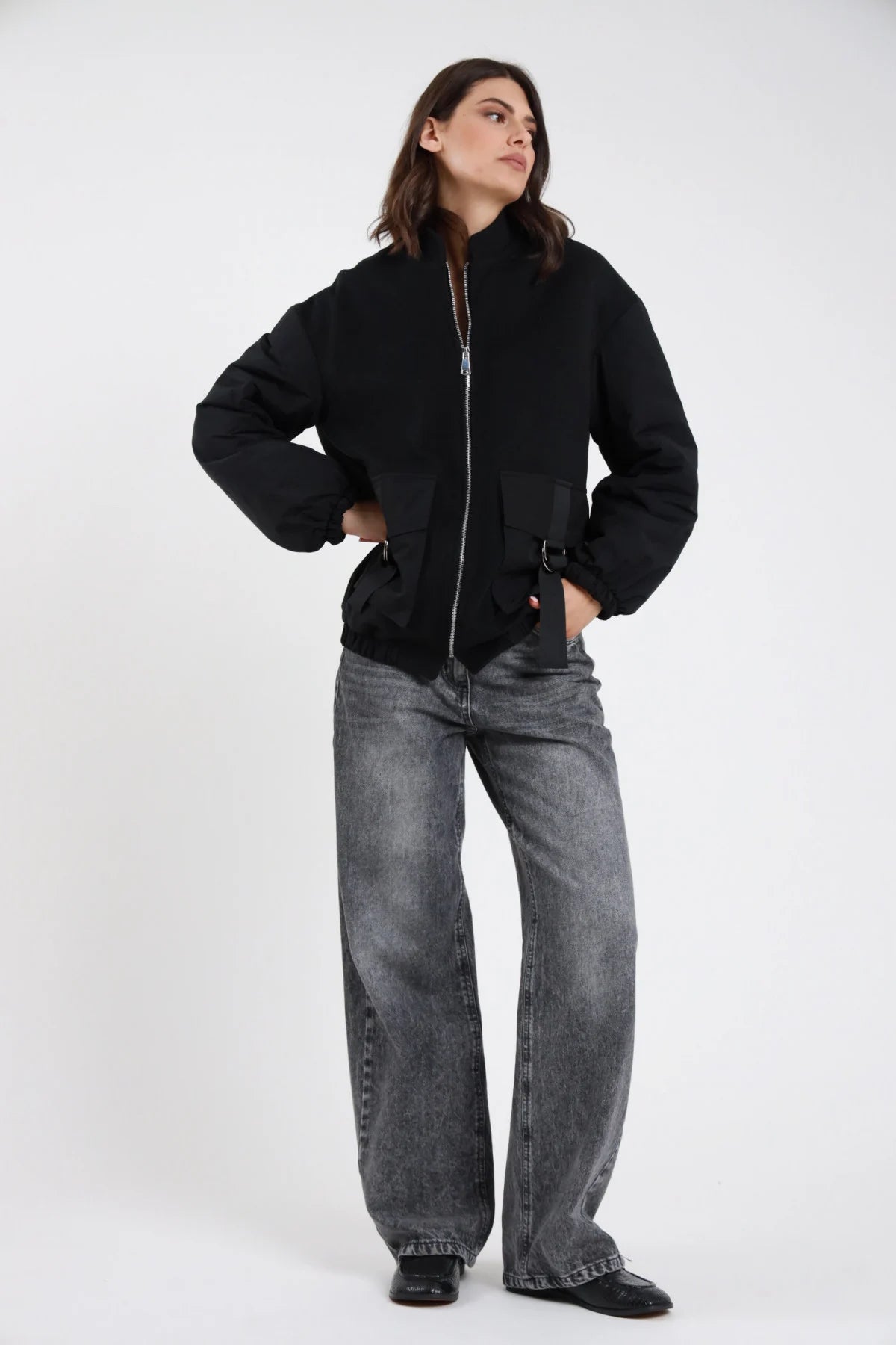 Jeans Mire straight leg wide leg grigio antracite stonewashed vita alta 5 tasche gamba larga maxi orlo grezzo frontale intera mani fianchi sguardo alto laterale - modella frontale intera mani fianchi sguardo alto laterale capelli castani scuri sfondo bianco bomber nero zip argento loafer neri