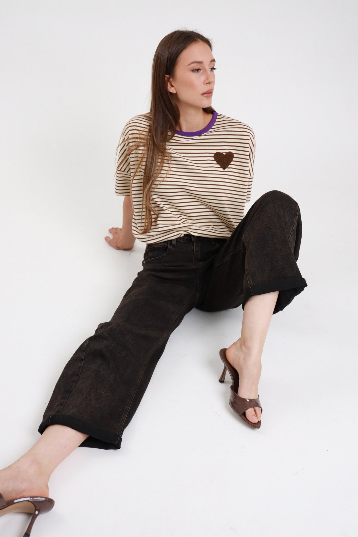 Jeans banana sabbiato nero donna Susy Mix – vita alta barrel leg vista seduta a terra con t-shirt righe cuore e sandali tacco