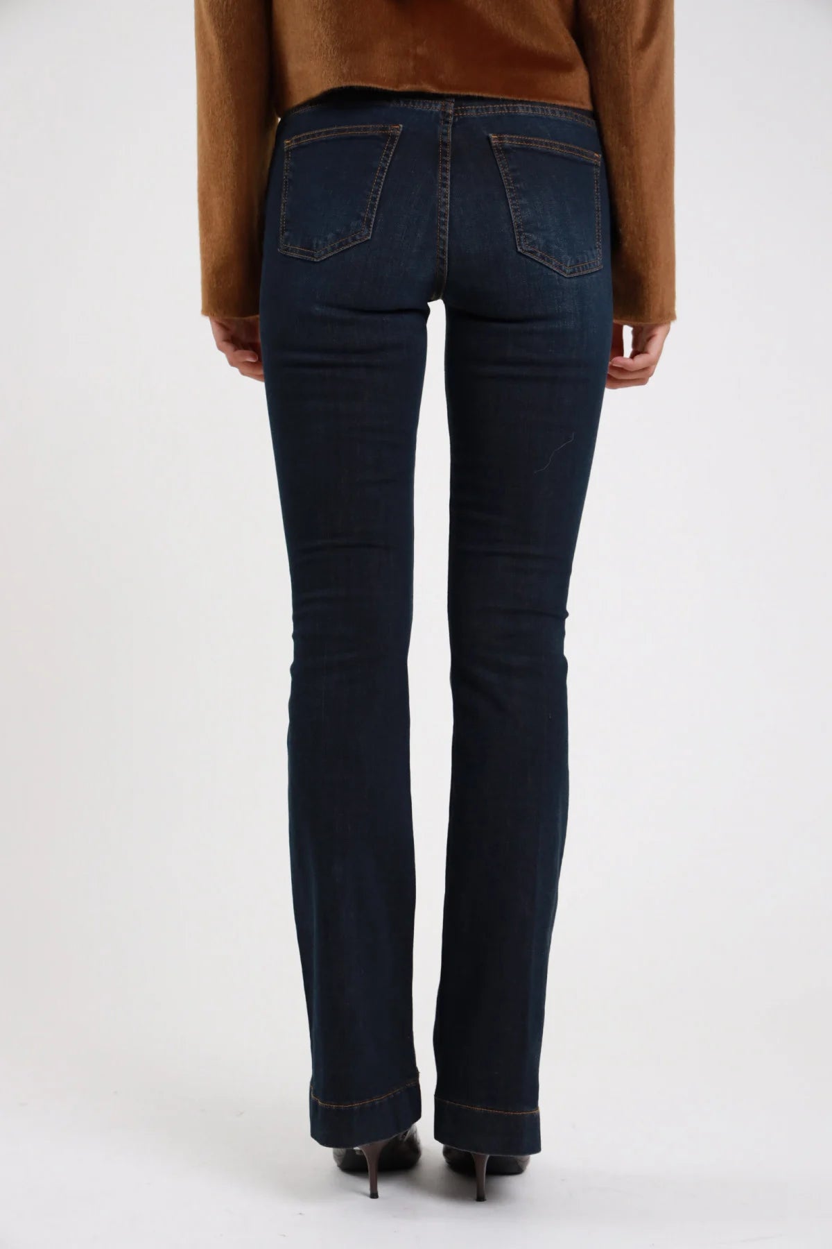 Jeans flare blu scuro dettaglio retro tasche classiche svasatura dal ginocchio - modella retro ravvicinata con maglia cioccolato e tacchi grigi