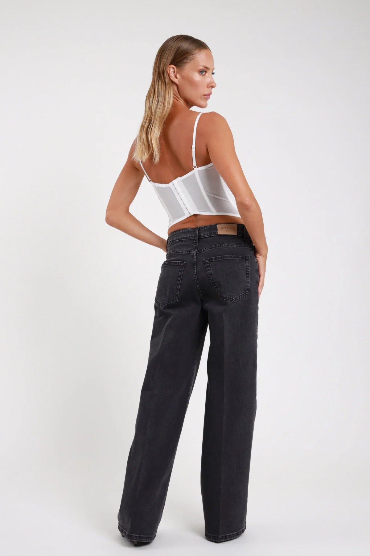Jeans palazzo wide-leg nero washed retro tre quarti gamba larga tasche retro - modella retro tre quarti sguardo posteriore top bustino bianco stivaletti tacco marrone capelli biondi lisci