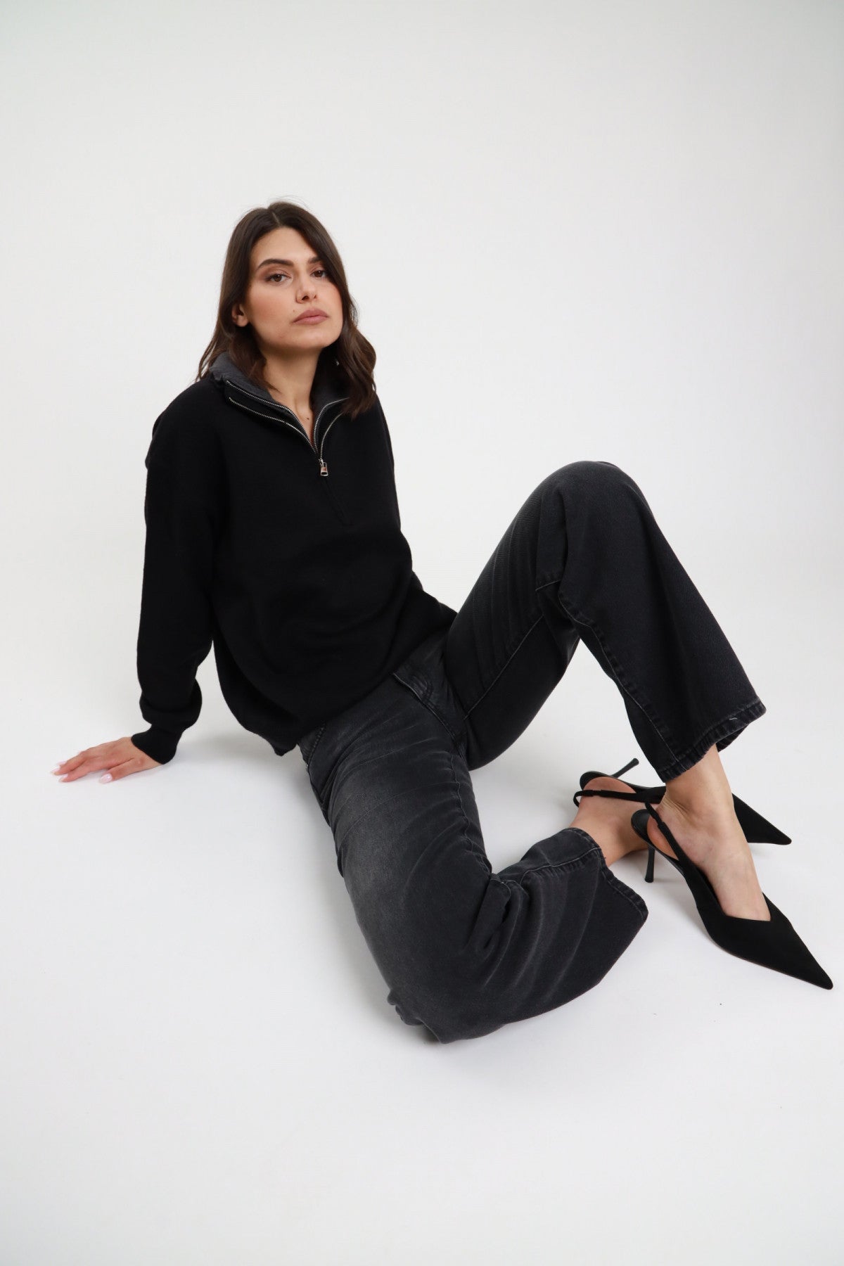 Jeans Debby Straight nero washed stone wash orlo grezzo raw hem gamba straight full length posa seduta terra - modella seduta terra gambe laterale sguardo frontale capelli castani sfondo bianco half-zip maglia nero décolleté nere