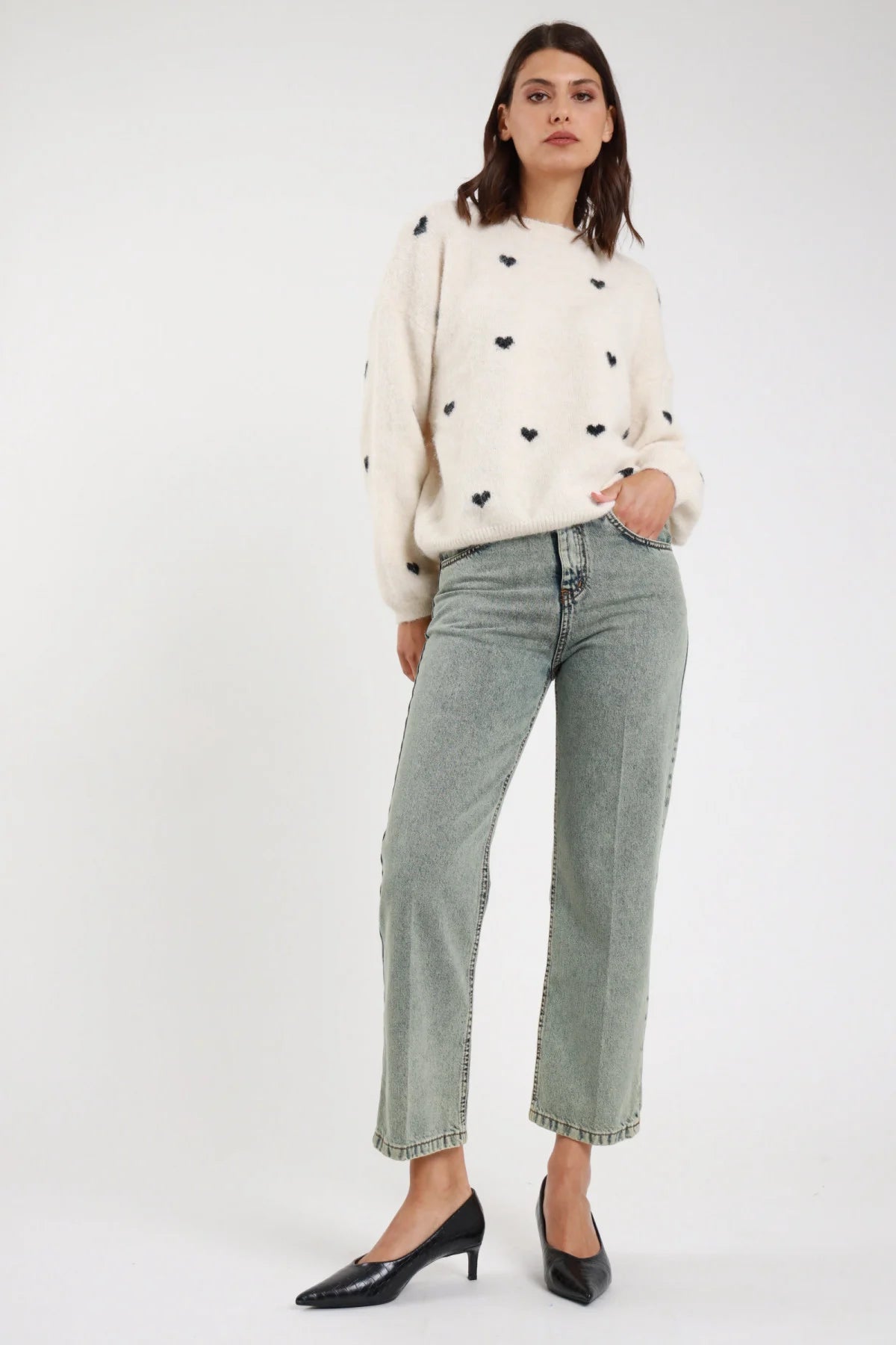 Jeans Manu straight leg verde sage acqua stonewashed rhinestone vita alta 5 tasche orlo grezzo frontale tre quarti mano tasca - modella frontale tre quarti mano tasca sguardo laterale capelli castani scuri mossi sfondo bianco pullover cuori avorio décolleté neri kitten heel