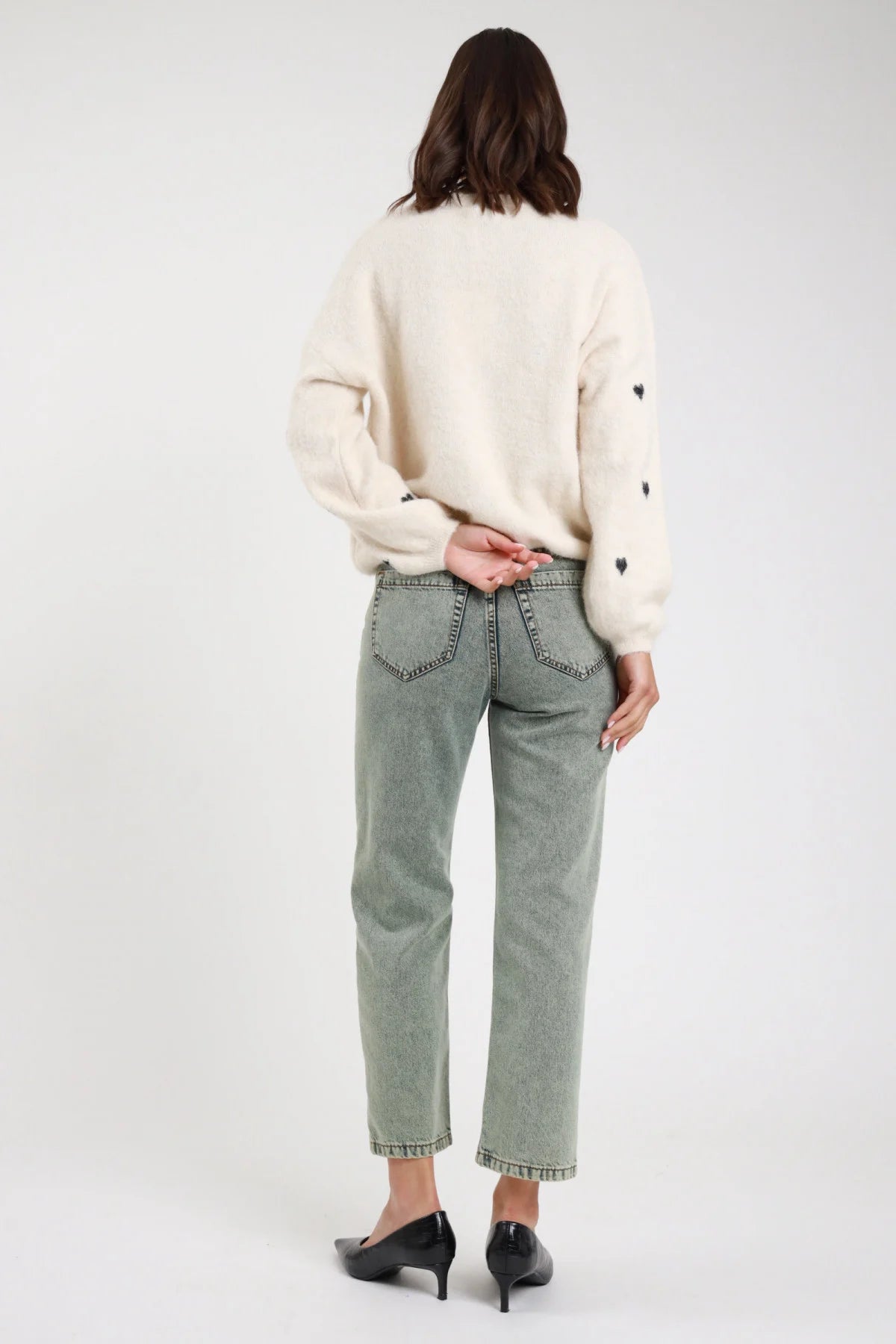 Jeans Manu straight leg verde sage acqua stonewashed rhinestone vita alta 5 tasche orlo grezzo retro intera mani intrecciate schiena - modella retro intera mani intrecciate schiena sguardo non visibile capelli castani scuri mossi sfondo bianco pullover cuori avorio décolleté neri kitten heel