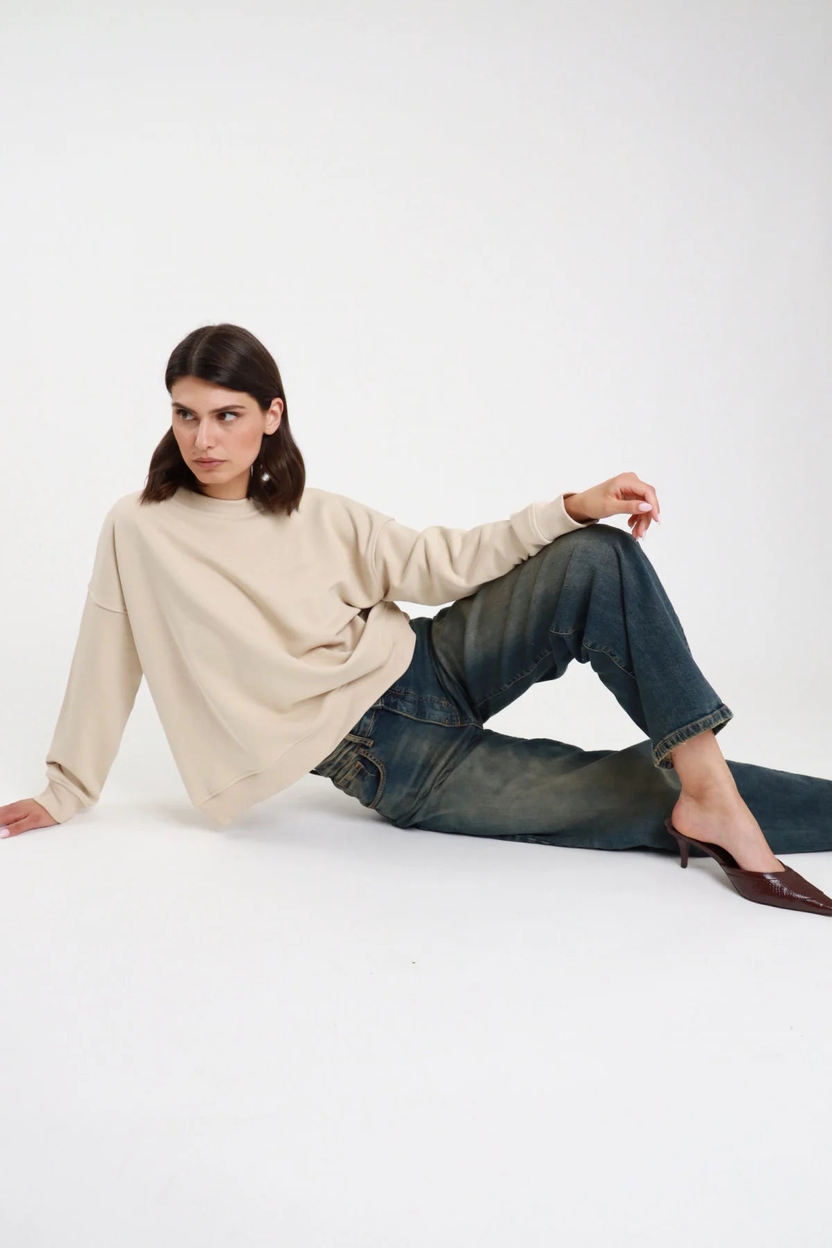 Jeans Eddie Wide Leg denim indaco blu petrol sovratinto vintage gamba larga wide leg volume orlo grezzo sfrangiato posa seduta terra laterale - modella seduta terra laterale sguardo laterale basso capelli castani scuri sfondo bianco felpa panna mule kitten heel marrone