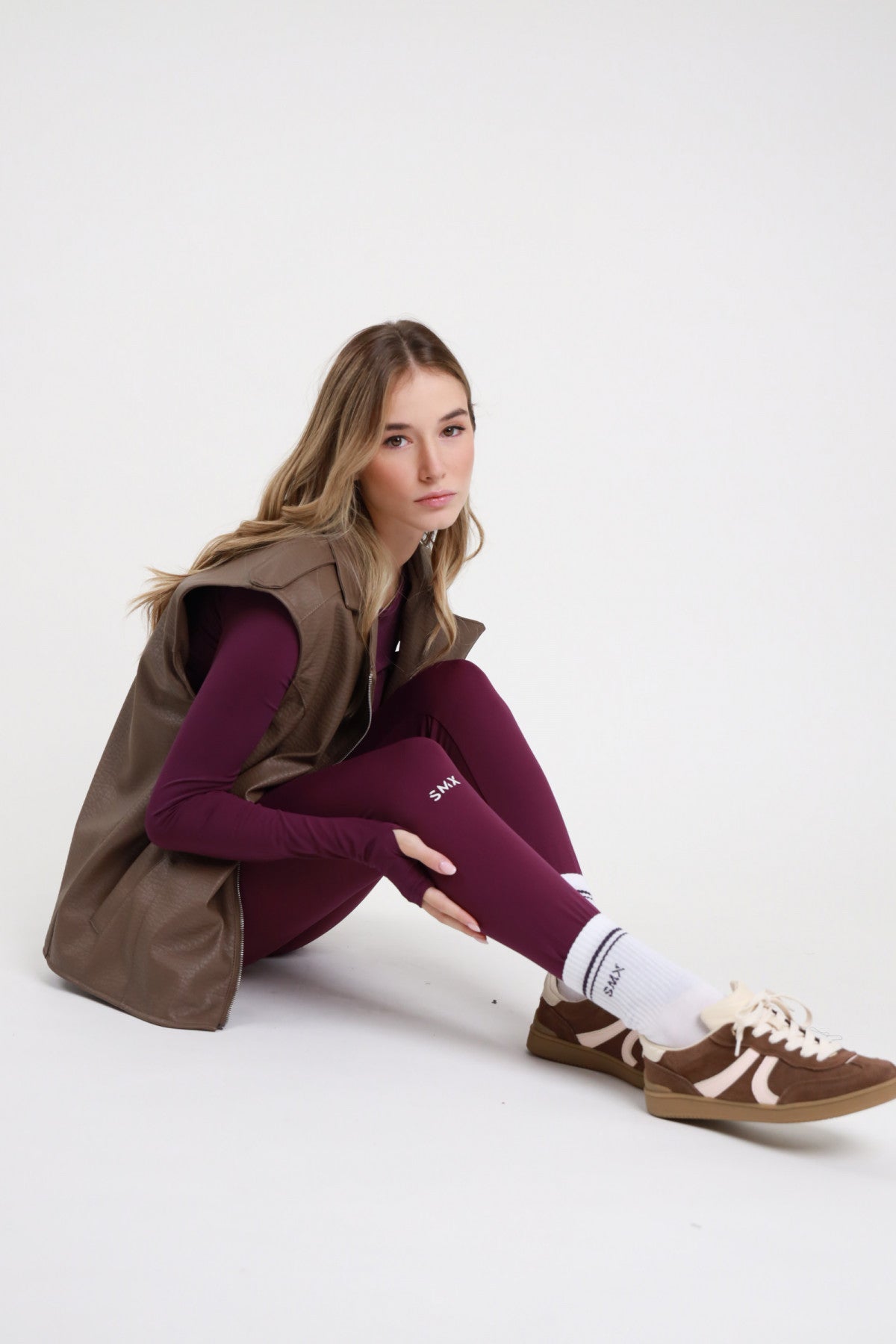 Leggings SMX Limited Edition viola melanzana vita alta logo SMX bianco coscia gamba laterale ben visibile full length seduta pavimento gambe avanti - modella seduta pavimento gambe avanti sguardo frontale capelli biondi mossi sfondo bianco logo SMX gamba chiaramente visibile gilet biker tortora maglia second skin viola calzini SMX bianchi sneakers Samba abbinati