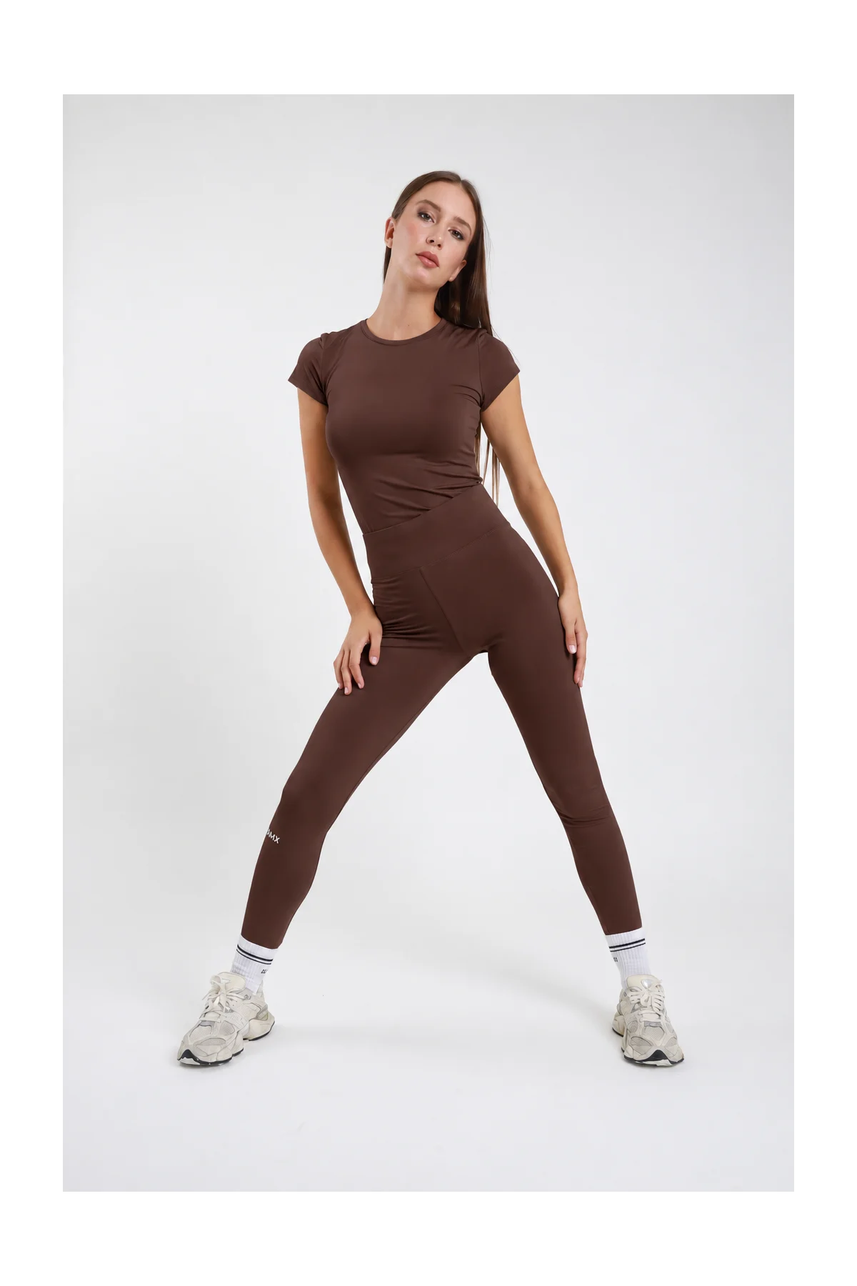 Leggings Body-Line DAYTHRU marrone cioccolato scuro vita alta elastica logo SMX polpaccio full-length second-skin frontale intera posa dinamica gambe aperte sguardo frontale - modella frontale intera posa dinamica gambe aperte sguardo frontale capelli castani lisci sfondo bianco t-shirt manica corta marrone coordinata sneakers bianche calze bianche SMX