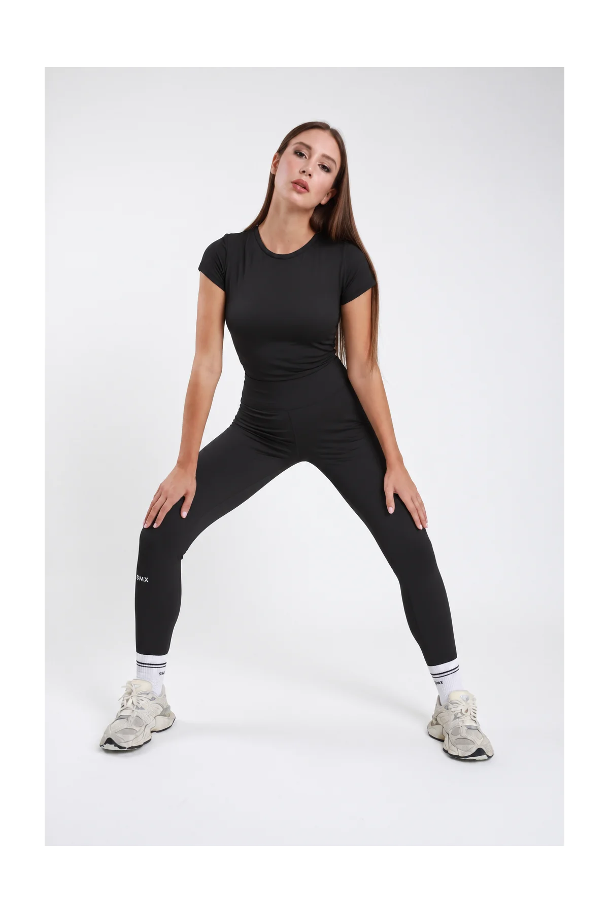 Leggings Body-Line DAYTHRU nero vita alta elastica logo SMX bianco polpaccio a contrasto full-length second-skin frontale intera posa dinamica gambe aperte sguardo frontale - modella frontale intera posa dinamica gambe aperte sguardo frontale capelli castani lisci sfondo bianco t-shirt manica corta nera coordinata sneakers bianche calze bianche SMX