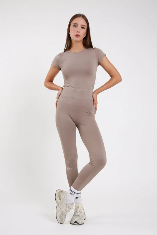 Leggings Body-Line DAYTHRU tortora taupe vita alta elastica logo SMX polpaccio full-length second-skin silhouette body-line frontale intera posa statica mani dietro schiena sguardo frontale - modella frontale intera posa statica mani dietro schiena sguardo frontale capelli castani lisci sfondo bianco t-shirt manica corta tortora coordinata sneakers beige calze bianche SMX