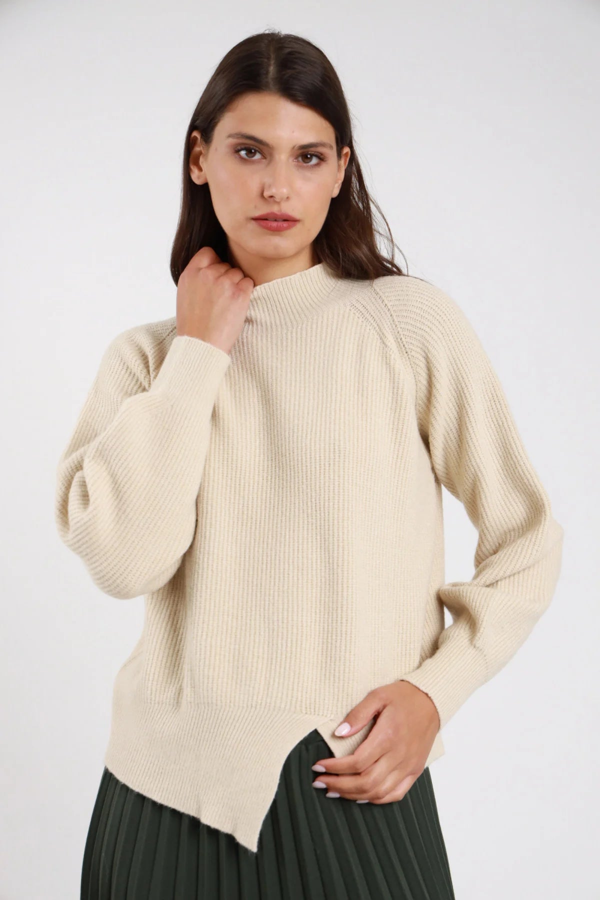 Pullover maglia coste mock neck collo semi-alto fondo asimmetrico spacco punta batwing oversize avorio ecru panna frontale tre quarti mano collo gonna verde scuro plissettata - modella frontale tre quarti mano collo sguardo frontale capelli castani scuri lisci sfondo bianco gonna verde scuro plissettata