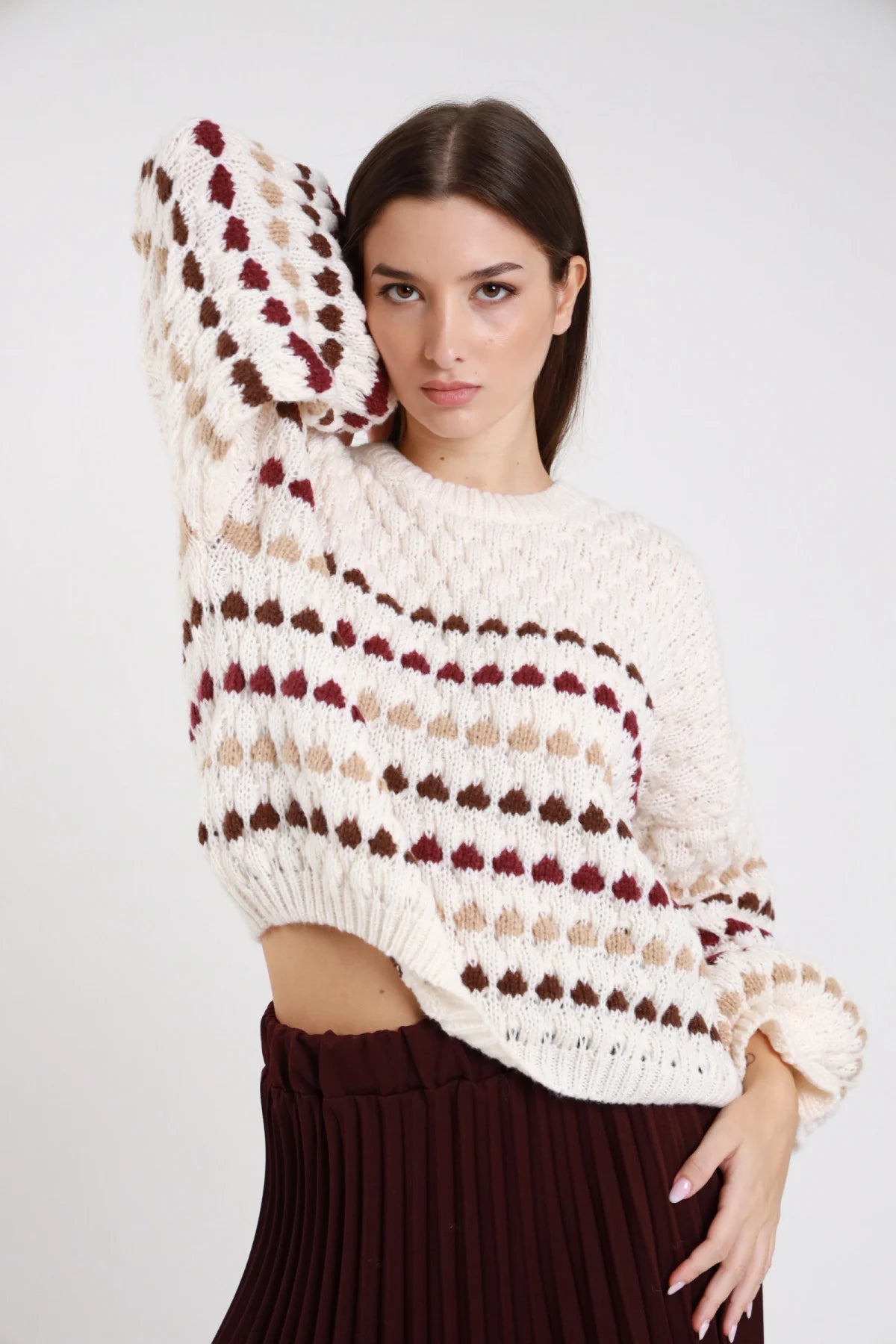 Maglione chunky knit panna ecru pois bolli tridimensionali rilievo righe orizzontali bordeaux cioccolato sabbia frontale busto braccio alzato testa girocollo manica balloon bishop polsino coste oversize boxy vita fondo coste - modella frontale busto braccio sinistro alzato mano testa sguardo frontale intenso capelli castani scuri lisci sfondo bianco gonna plissé bordeaux