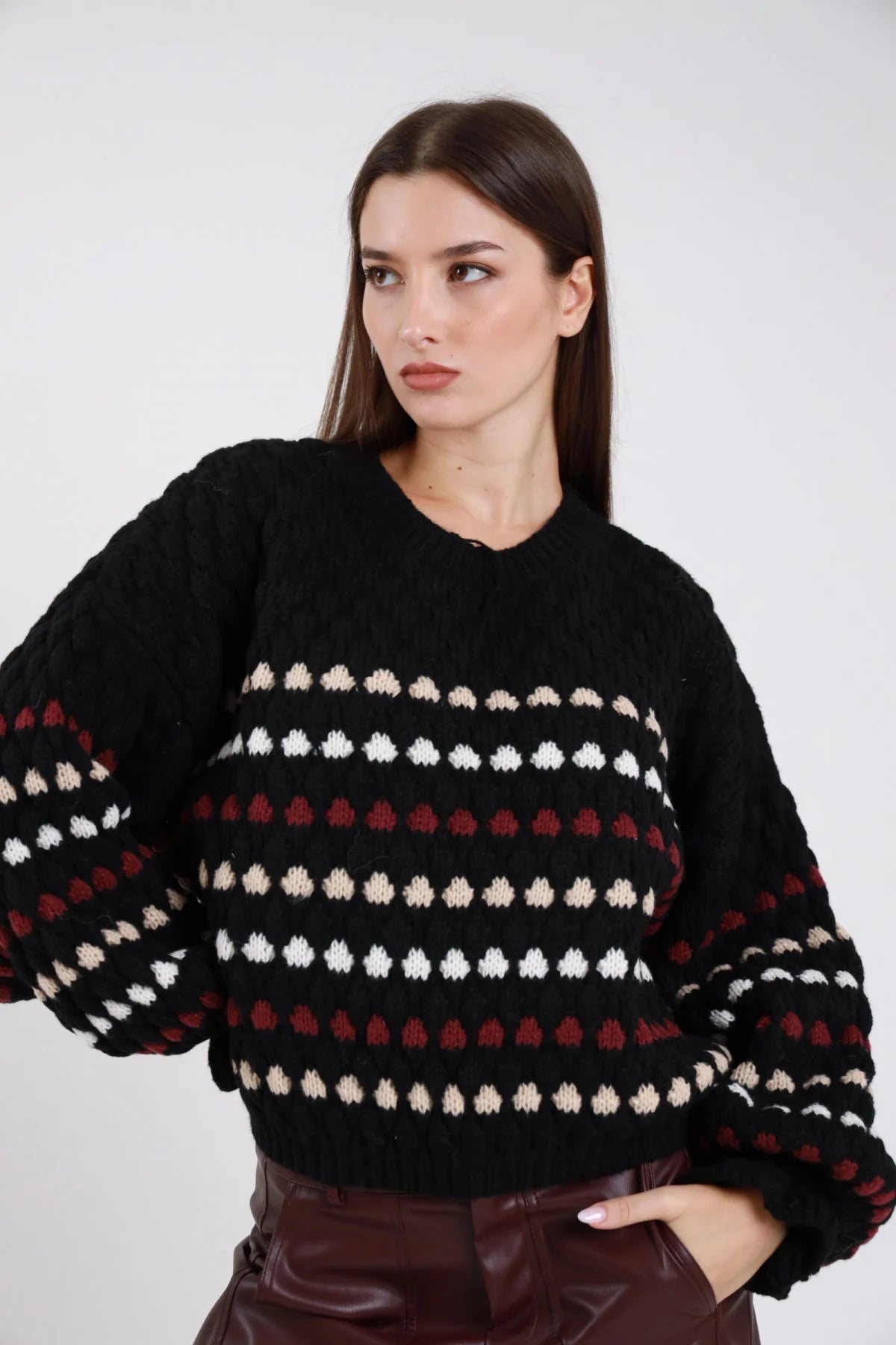 Maglione chunky knit nero pois bolli tridimensionali rilievo righe orizzontali panna bordeaux frontale busto mani fianchi girocollo manica balloon bishop polsino coste oversize boxy vita fondo coste - modella frontale busto mani fianchi sguardo laterale alto capelli castani scuri lisci sfondo bianco pantaloni bordeaux in pelle lucida