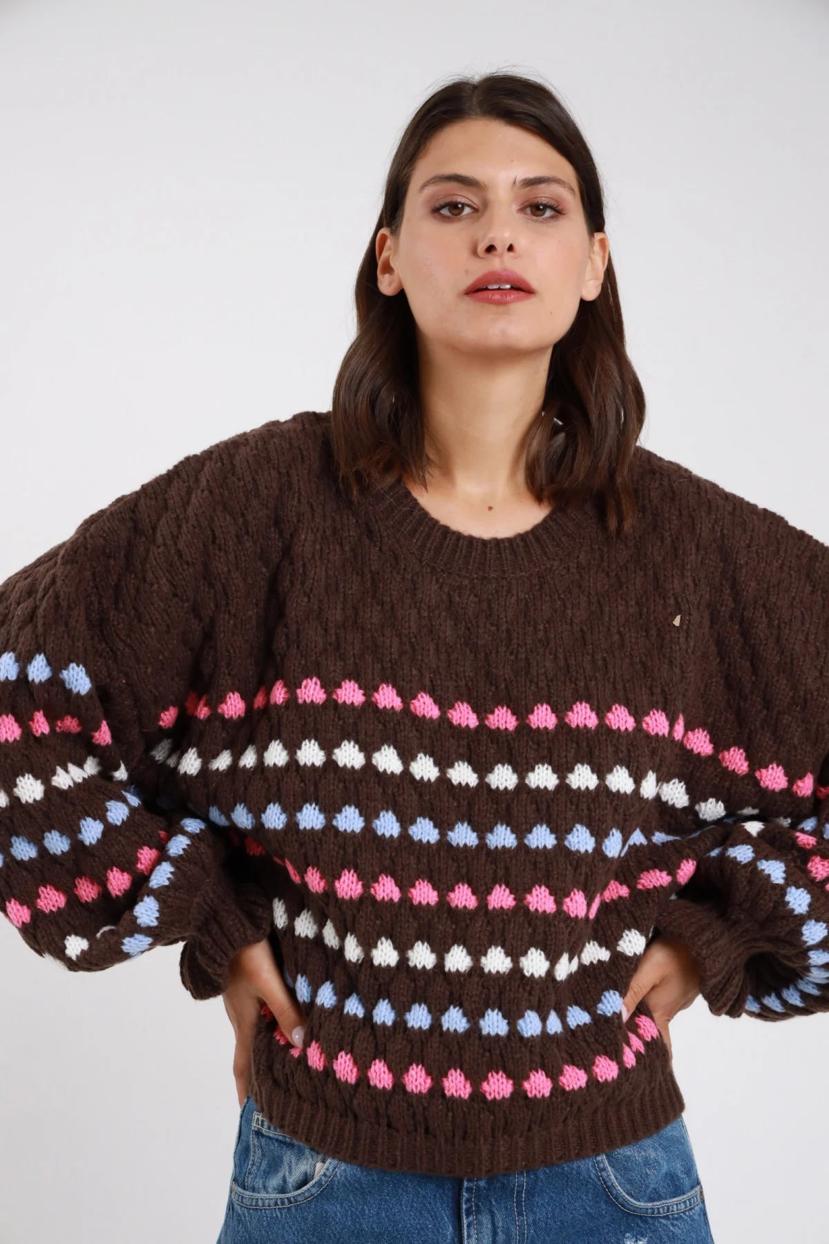 Maglione chunky knit cioccolato moro scuro pois bolli tridimensionali rilievo righe orizzontali rosa azzurro panna frontale busto mani fianchi girocollo manica balloon bishop polsino coste oversize boxy vita fondo coste - modella frontale busto mani fianchi sguardo frontale intenso capelli castani medi mossi sfondo bianco jeans denim blu