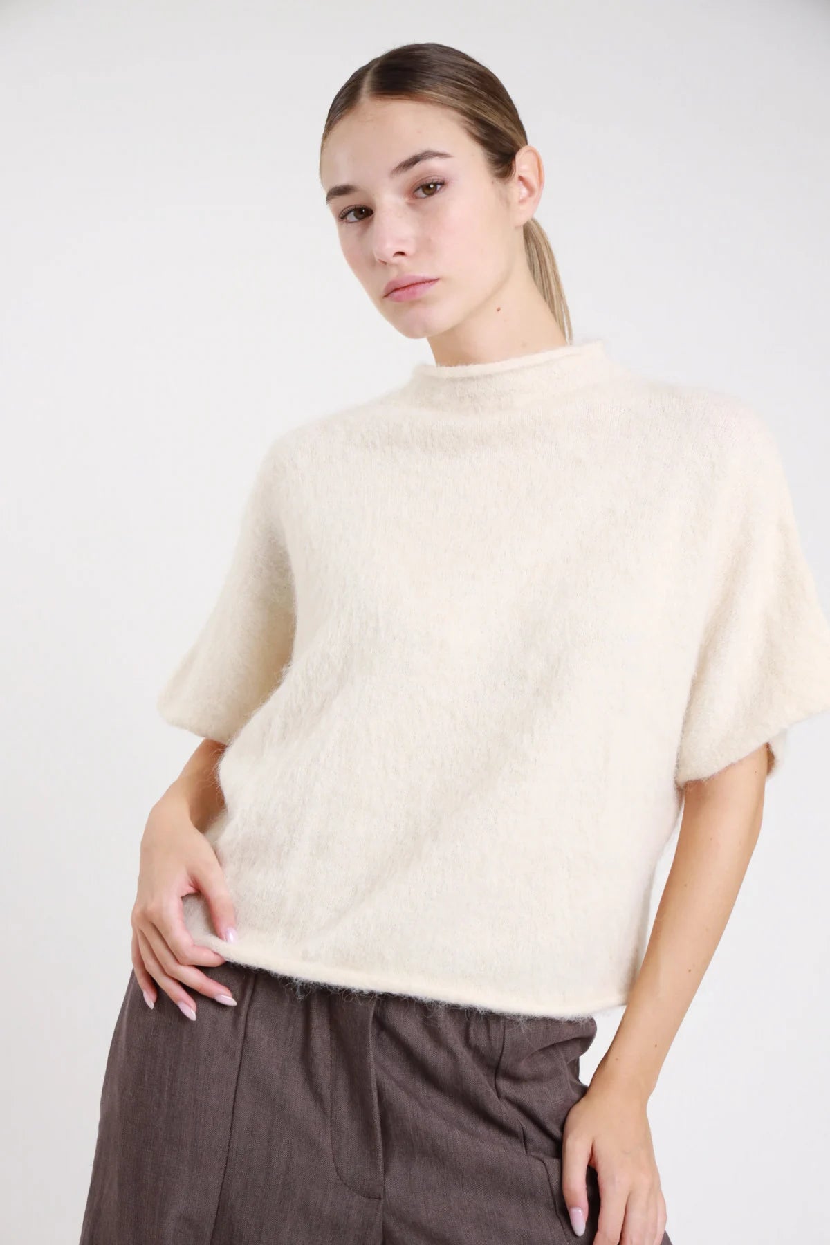 Pullover maniche corte rosa bubblegum candy pink maglia mohair spazzolata mock-neck crop - modella busto frontale mano al mento sguardo frontale gonna grigio scuro capelli castani raccolti