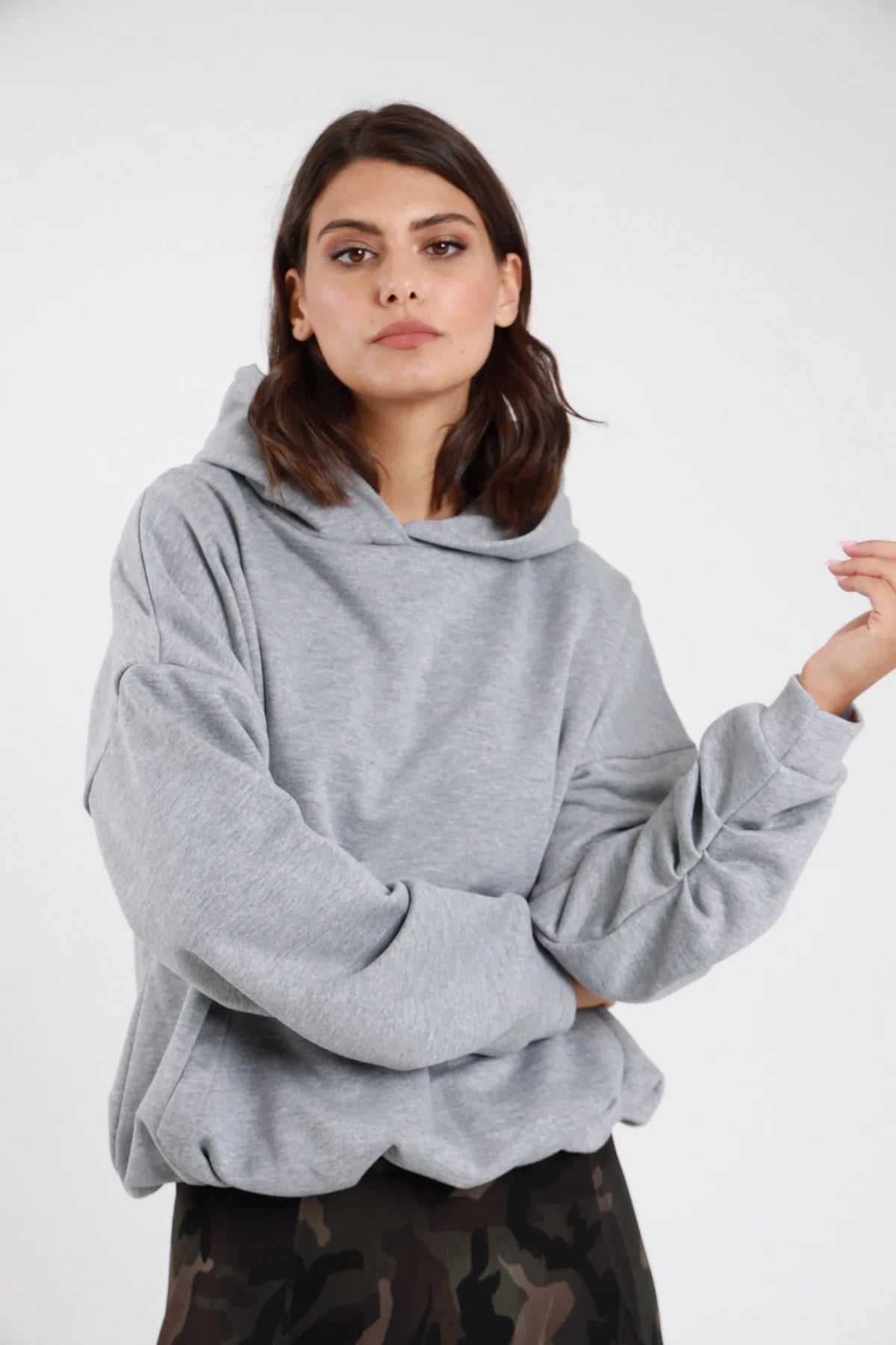 Felpa cappuccio grigio mélange donna oversize cropped cappuccio ampio tasca marsupio polsino costine - dettaglio frontale mezzo busto mani incrociate con gonna mimetica