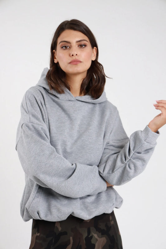 Felpa cappuccio grigio mélange donna oversize cropped cappuccio ampio tasca marsupio polsino costine - dettaglio frontale mezzo busto mani incrociate con gonna mimetica
