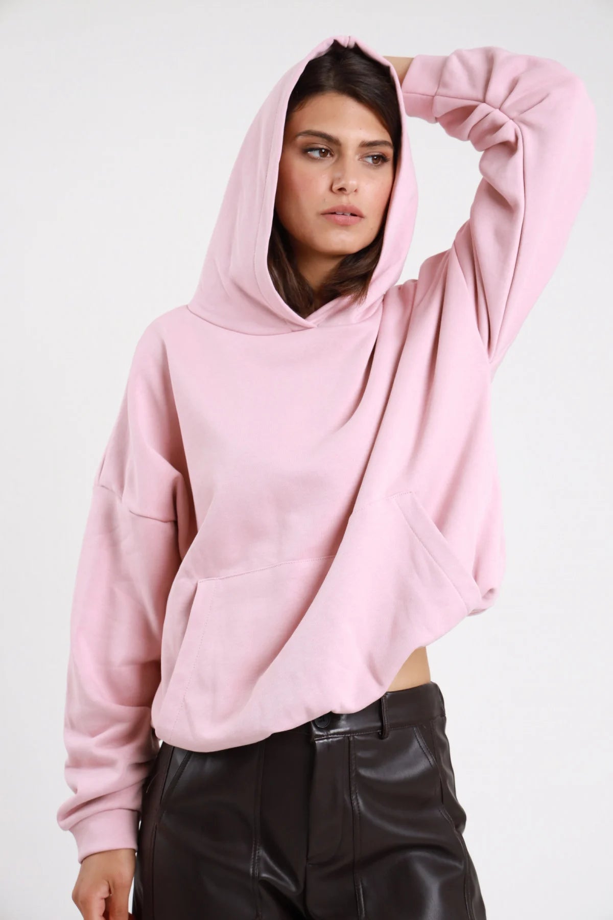 Felpa cappuccio rosa cipria donna oversize cropped cappuccio ampio tasca marsupio maniche lunghe - vista frontale tre quarti mano al cappuccio con pantaloni neri ecopelle