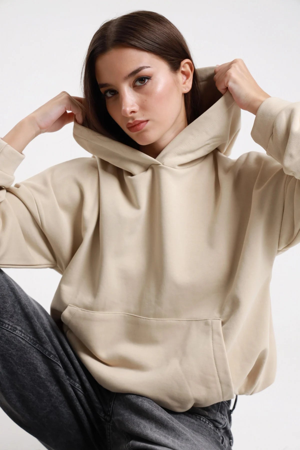 Felpa cappuccio beige sabbia donna oversize cropped cappuccio ampio tasca marsupio polsino costine - dettaglio frontale mezzo busto mani al cappuccio con jeans grigi