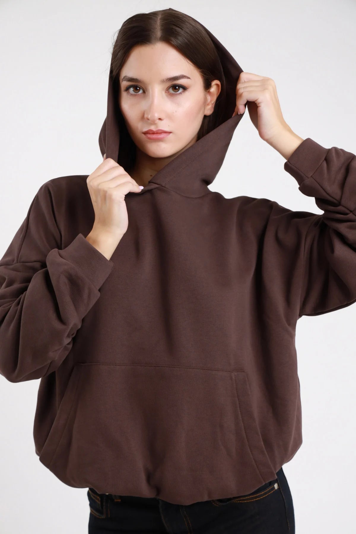 Felpa cappuccio marrone cioccolato donna oversize cropped cappuccio ampio tasca marsupio maniche lunghe - dettaglio frontale mezzo busto mani al cappuccio con jeans neri