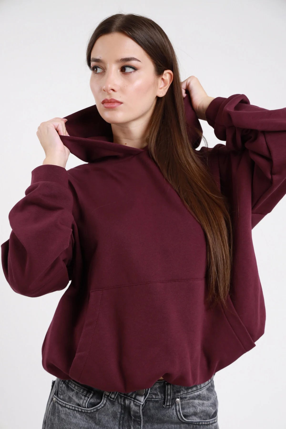 Felpa cappuccio bordeaux vinaccia donna oversize cropped cappuccio ampio tasca marsupio fondo arrotondato - dettaglio frontale mezzo busto mani al cappuccio con jeans grigi